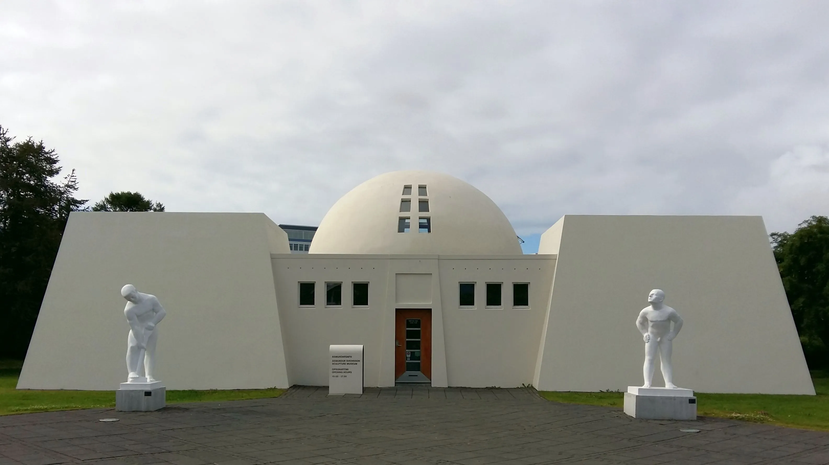 Edificio blanco con cúpula y dos grandes esculturas blancas flanqueando la entrada en Ásmundarsafn