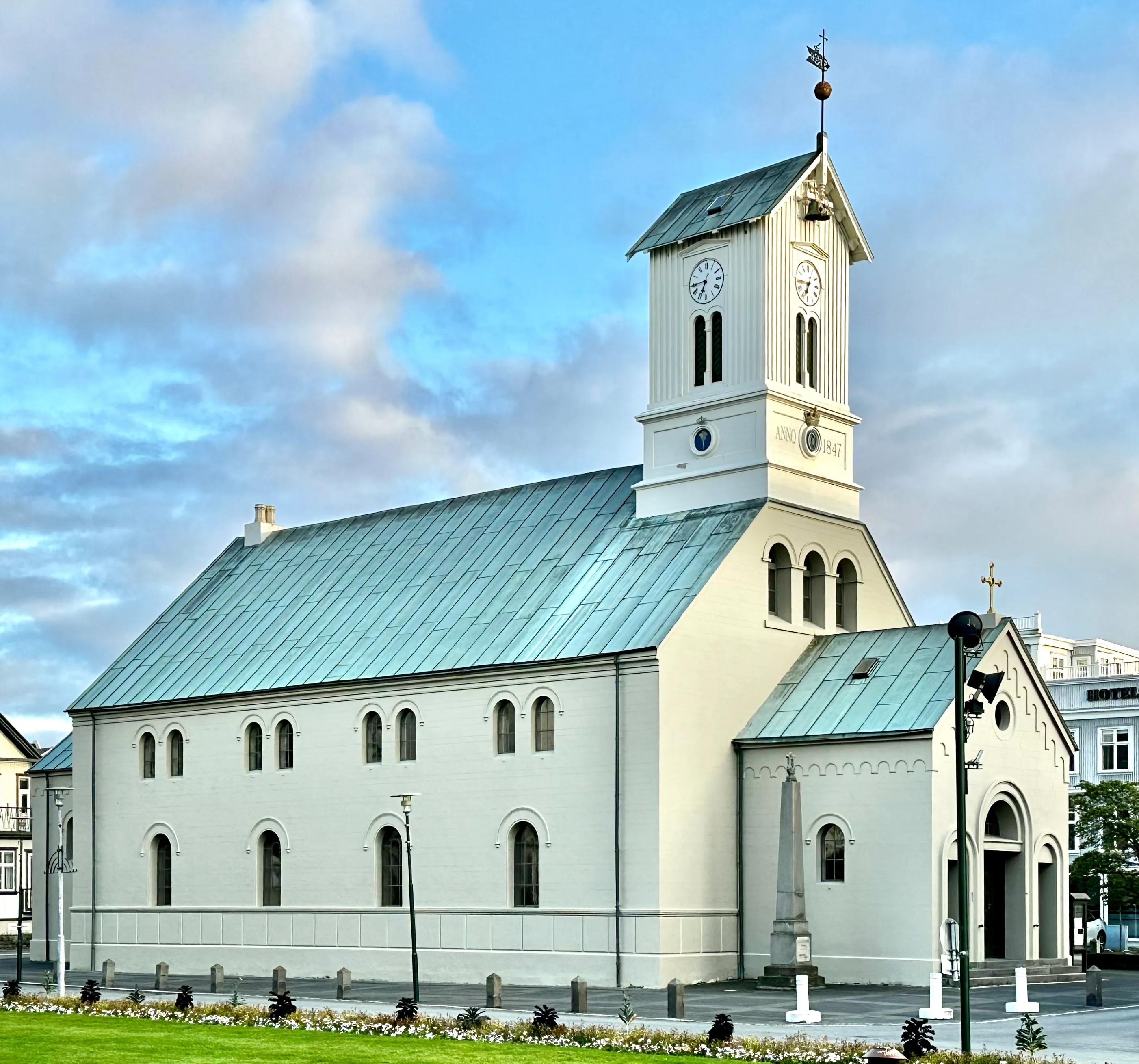 Witte neoklassieke kerk met een klokkentoren en een groen metalen dak onder een bewolkte blauwe lucht
