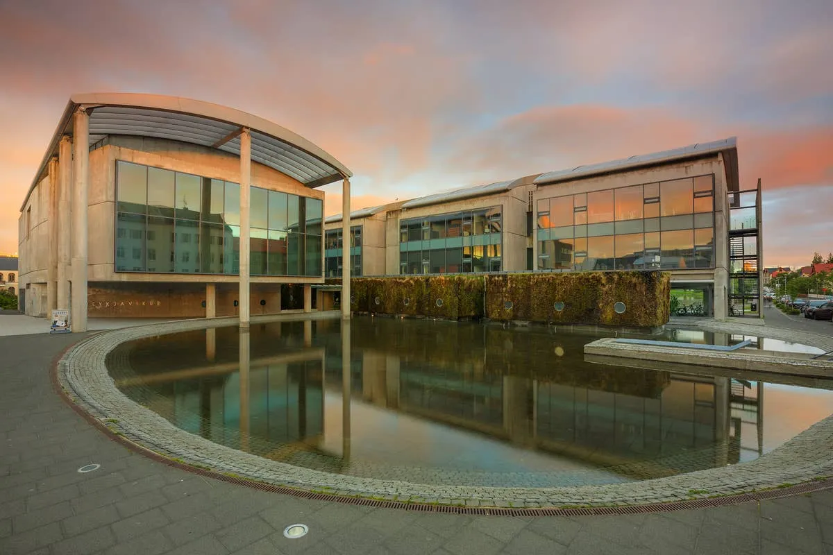 Edificio moderno de cristal y hormigón con un techo curvo que se refleja en un gran estanque circular al atardecer