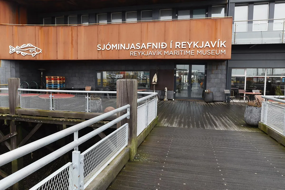 Wooden facade of the Reykjavík Maritime Museum with a fish logo and a walkway leading to the glass entrance doors.
