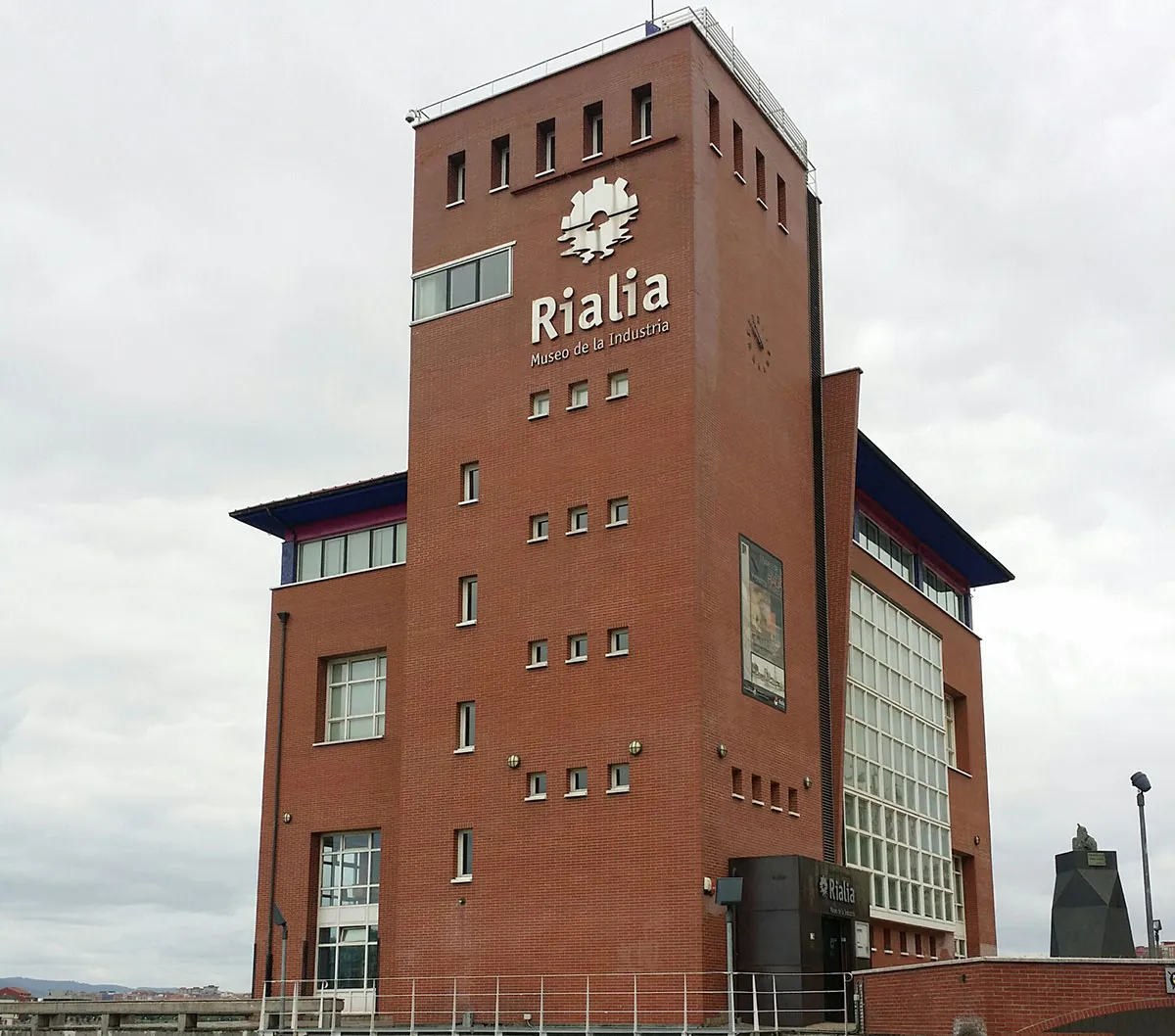 Alto edificio de torre de ladrillo rojo con el letrero Rialia Museo de la Industria y un emblema blanco en la fachada.