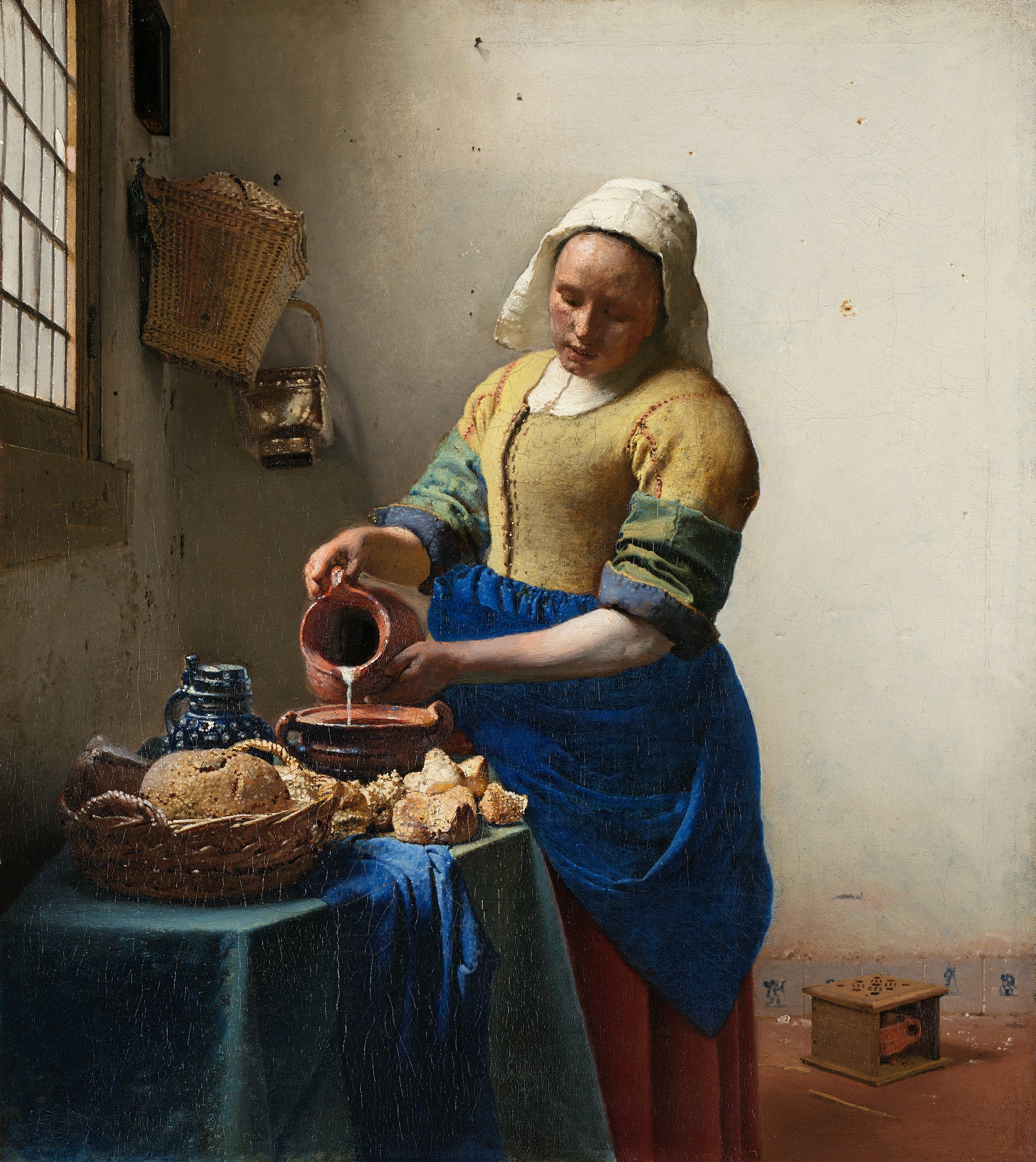 Vrouw in geel en blauwe jurk giet melk in kom in een eenvoudige Nederlandse keuken met brood op tafel