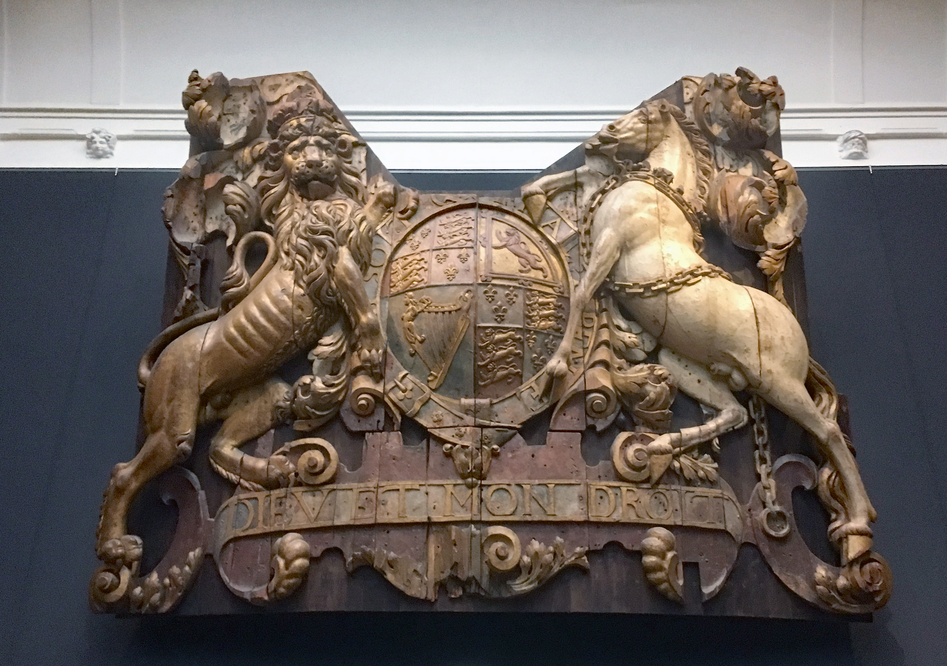 Ornate wooden coat of arms with a lion and horse flanking a shield and inscribed text