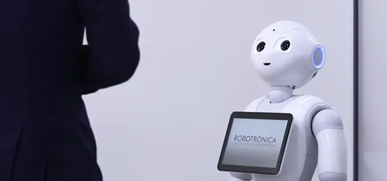 A white humanoid robot with a screen displaying 'ROBOTRONICA' stands next to a person in a dark suit.