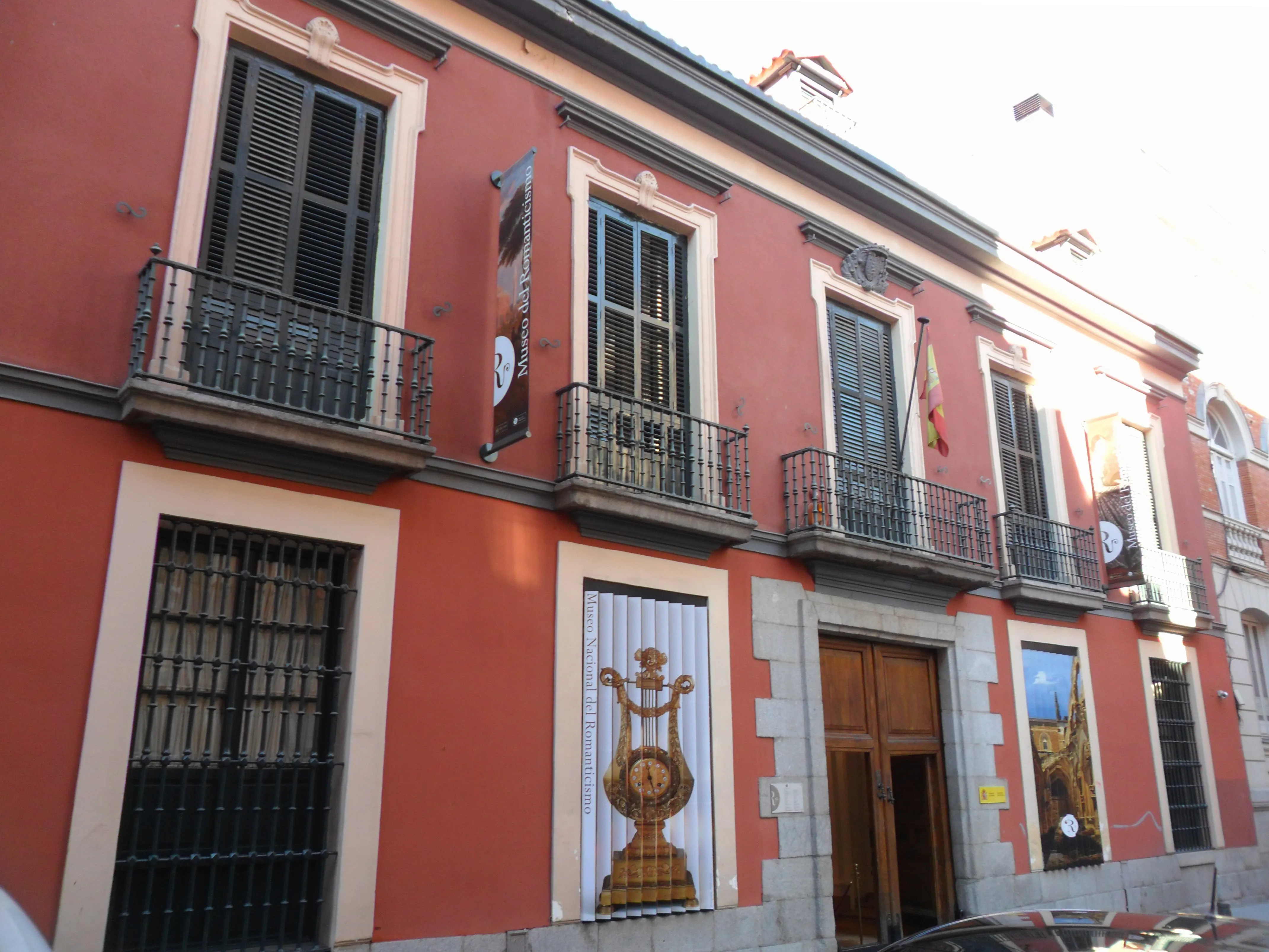 Fachada de edificio rojo con molduras blancas, balcones negros y un gran letrero de lira sobre la entrada