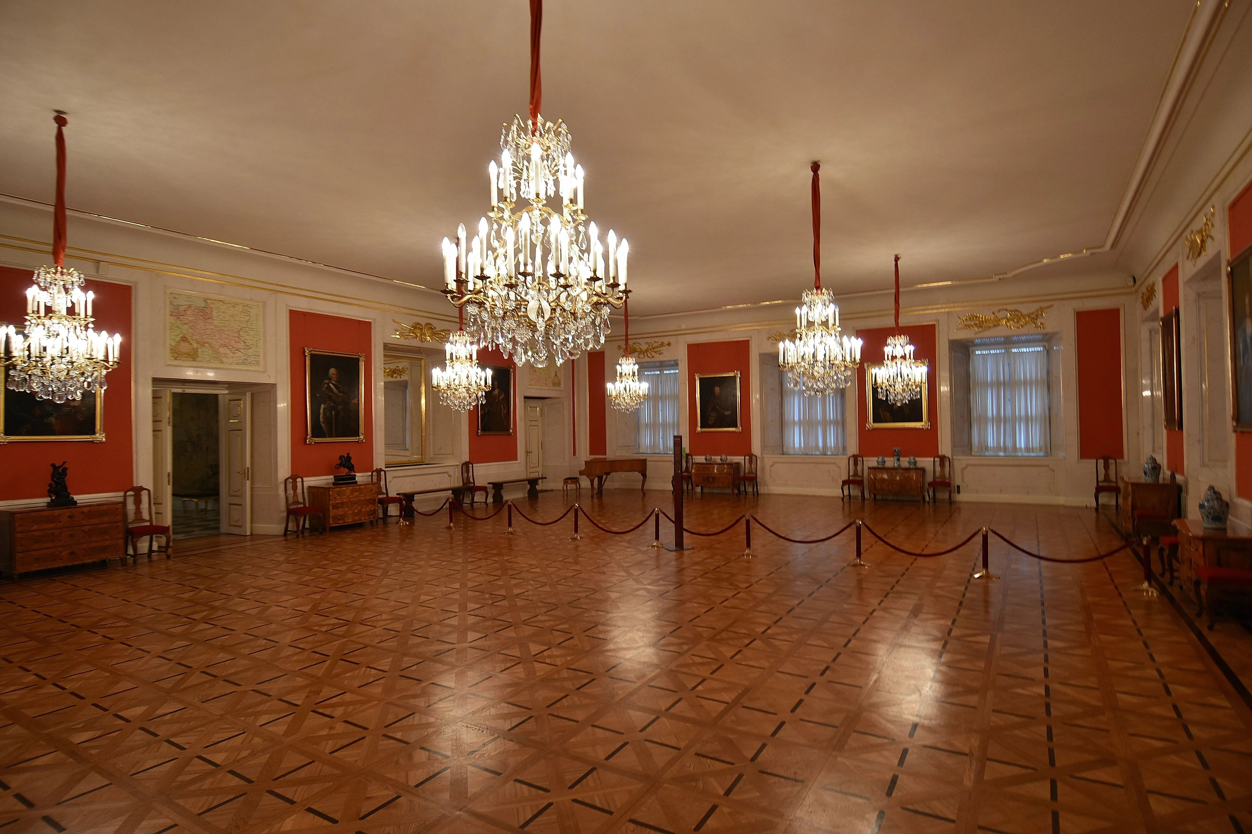 grote kamer met hoge plafonds, sierlijke kroonluchters, rode muren en een houten vloer