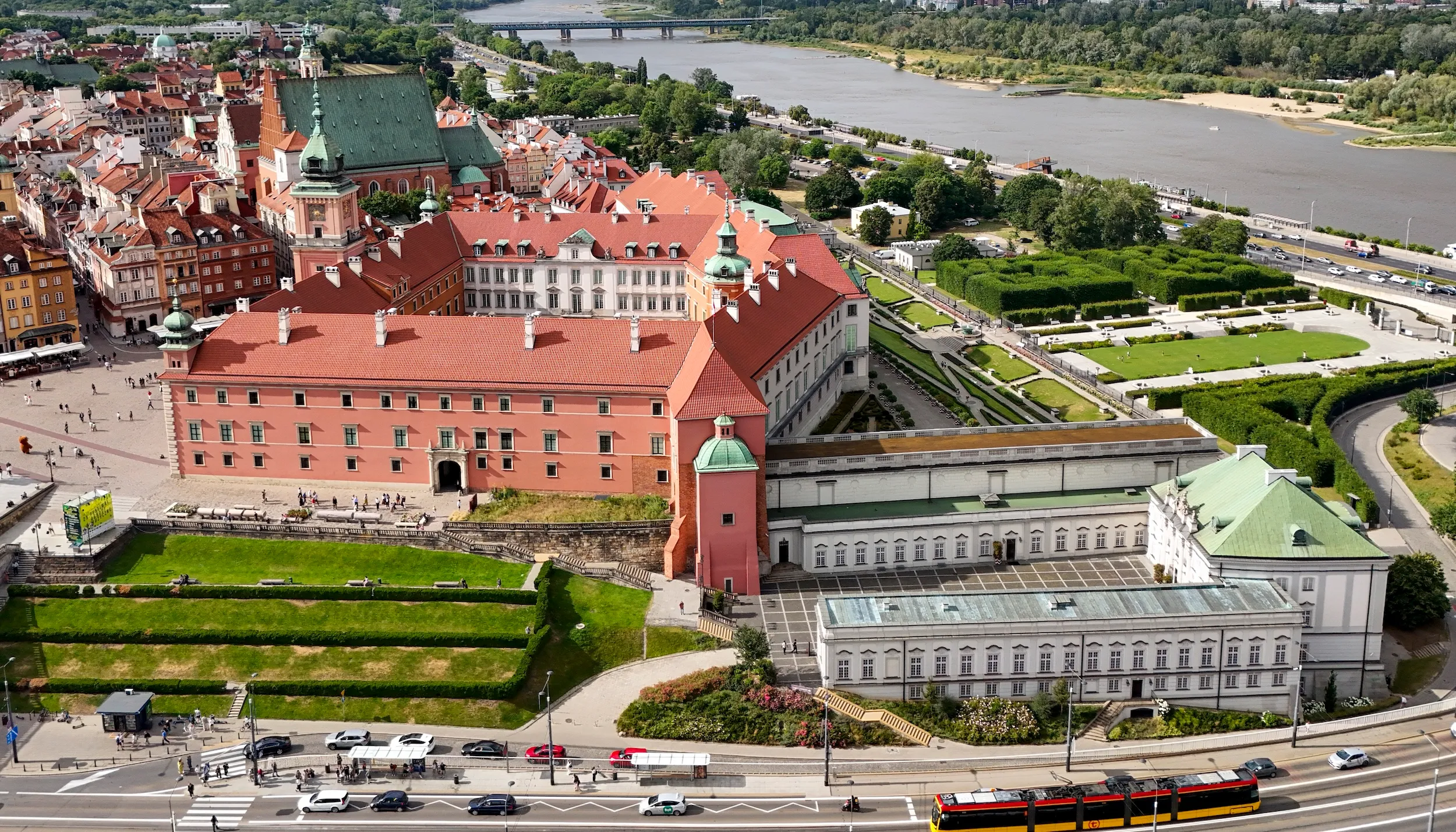 Widok z lotu ptaka na Zamek Królewski w Warszawie z budynkami o czerwonych dachach, zielonymi ogrodami i rzeką Wisłą