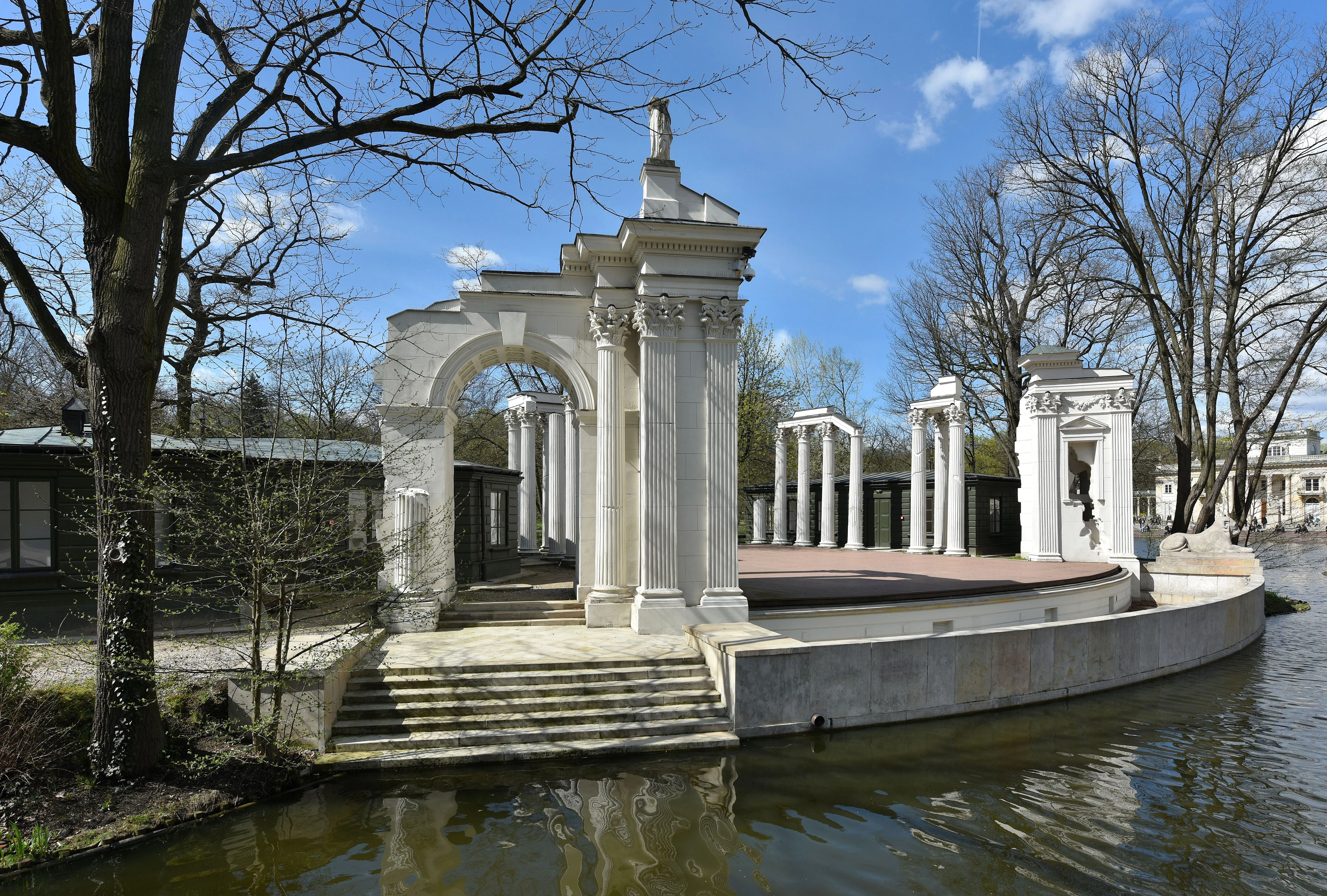Neoclassiek amfitheater met witte zuilen en trappen die leiden naar een waterpartij in een parksetting