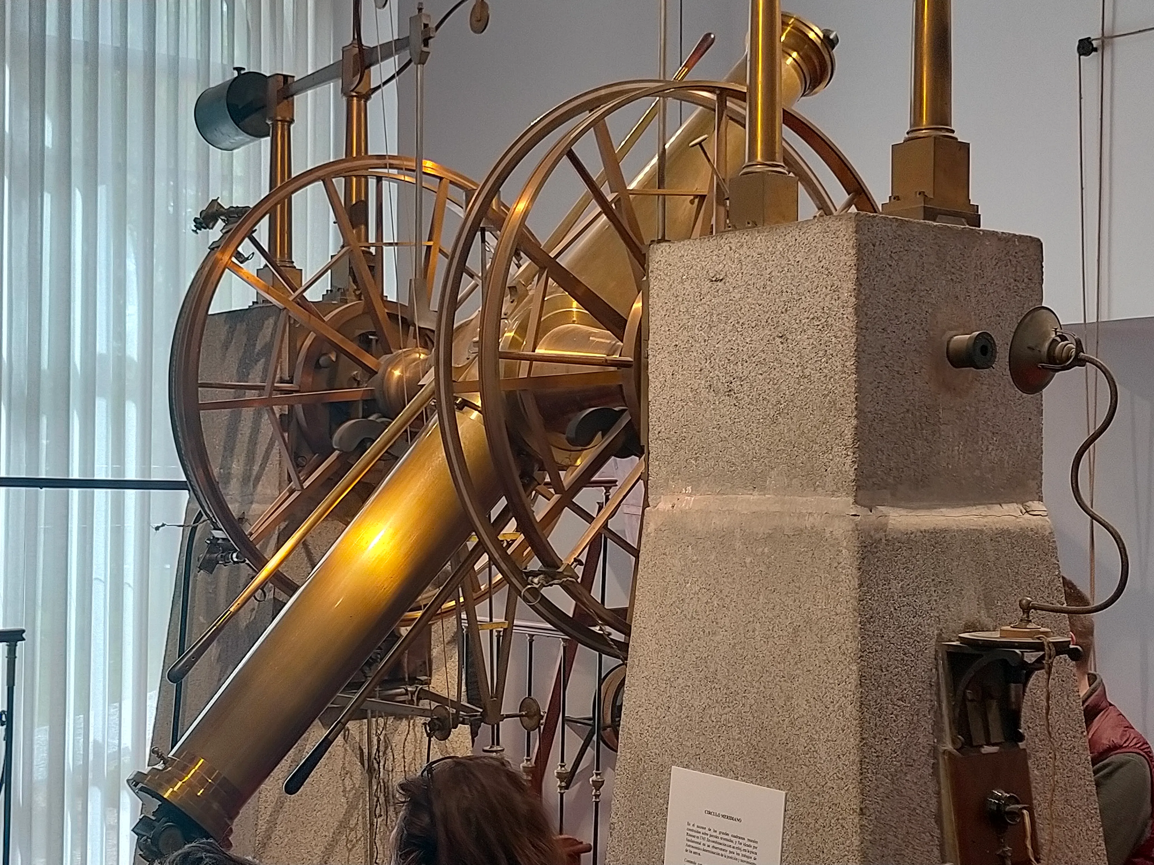 Duży zabytkowy teleskop z mosiężnymi i drewnianymi elementami, wyeksponowany na kamiennym postumencie w muzeum