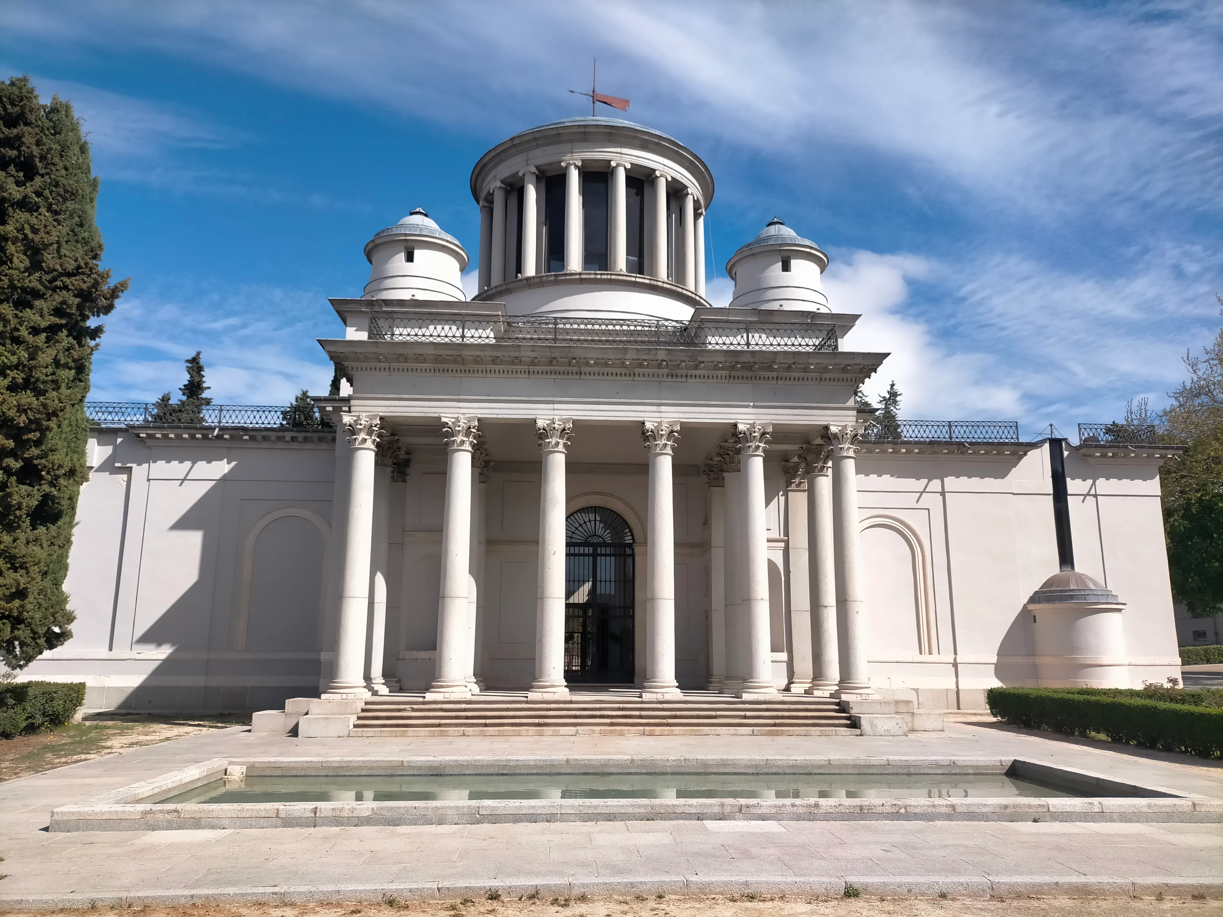 Budynek neoklasycystyczny z centralną kopułą i kolumnami, na tle błękitnego nieba z chmurami