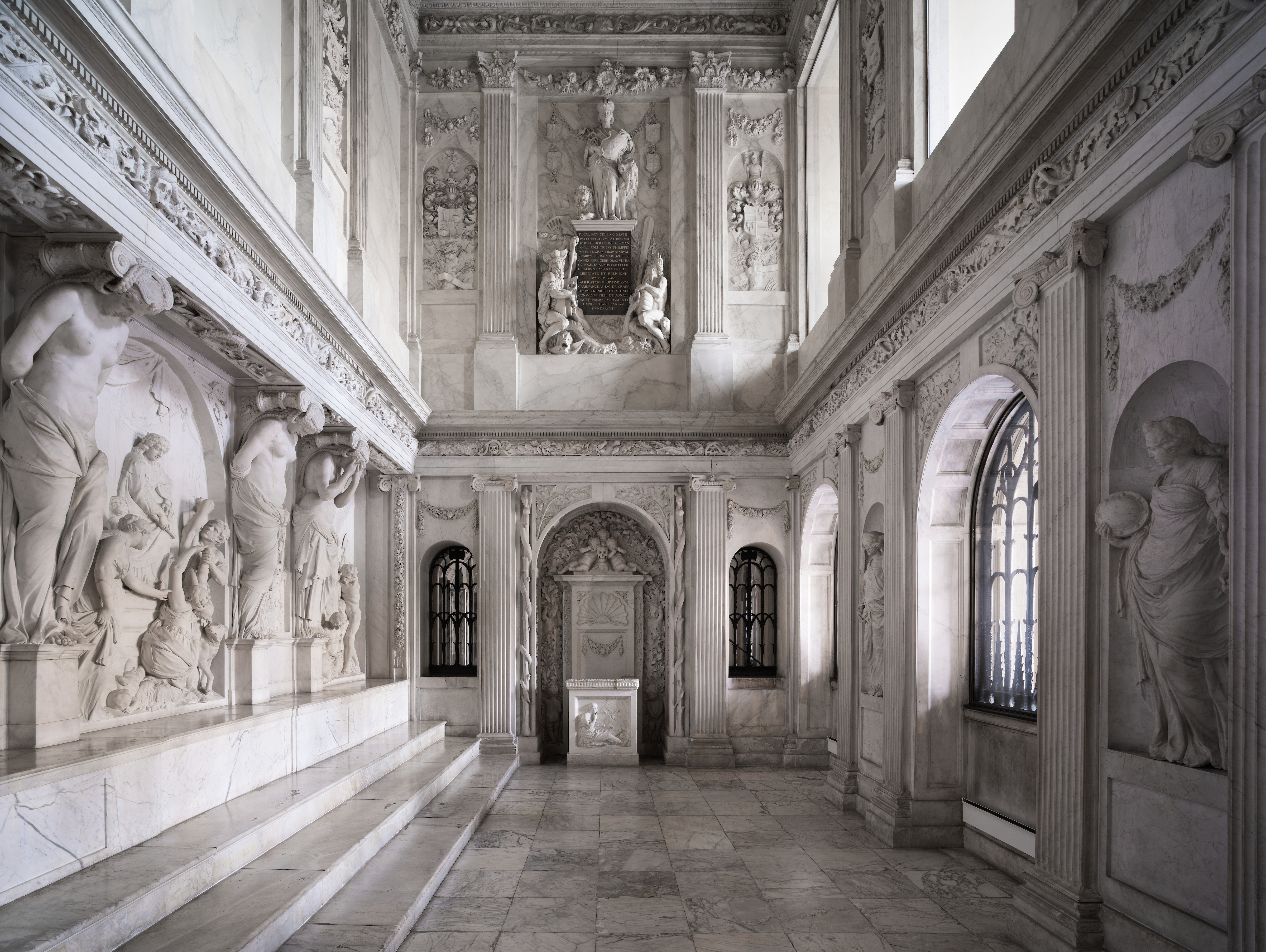 Gran sala con suelos de mármol, detalladas tallas en piedra y esculturas clásicas a lo largo de las paredes dentro del Palacio Real de Ámsterdam