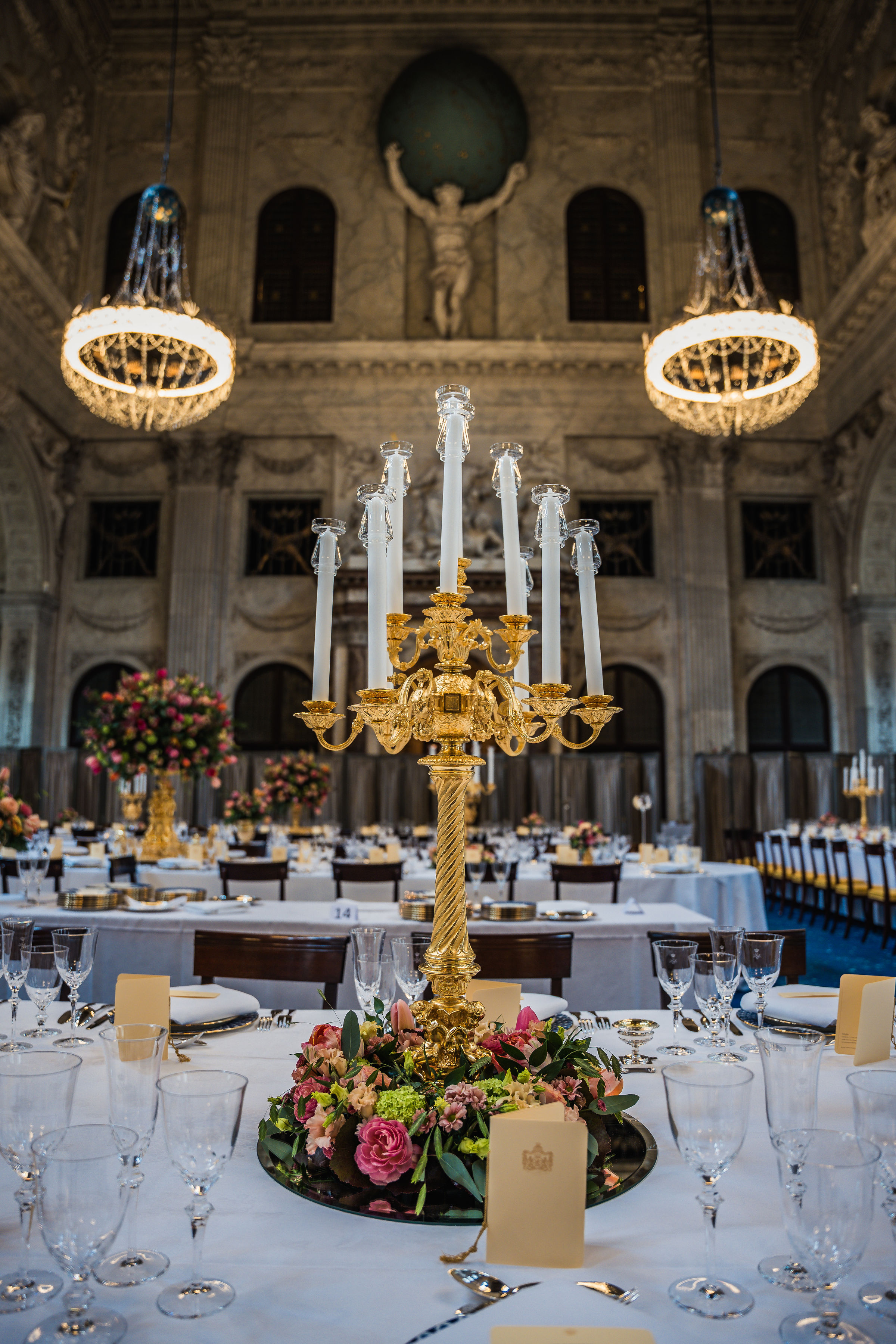Gran salón en el Palacio Real de Ámsterdam con candelabros dorados ornamentados, mesas vestidas de blanco, arreglos florales y techos altos decorativos