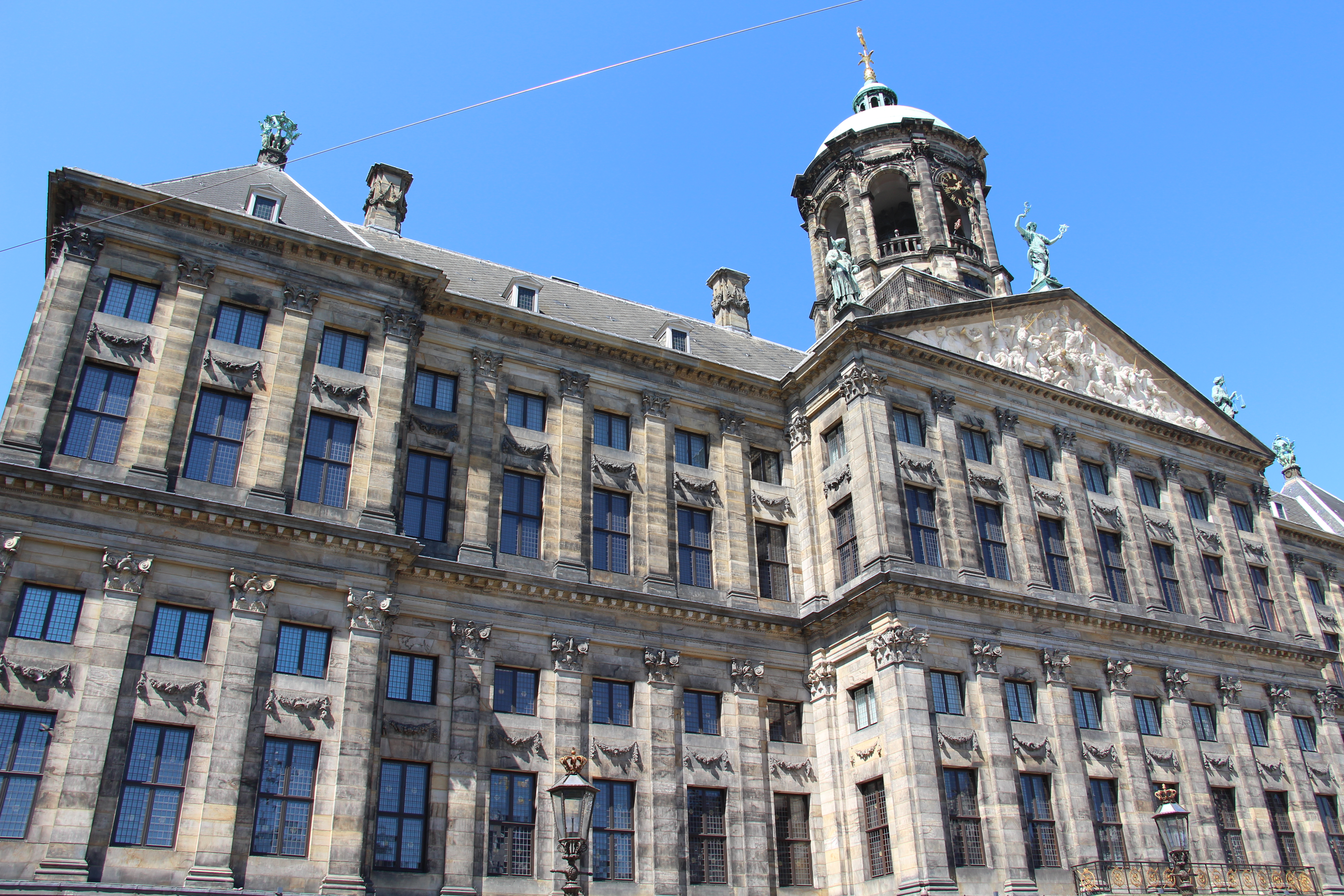 Grand facade of the Royal Palace Amsterdam with symmetrical windows, stone carvings, and a central dome under a clear blue sky