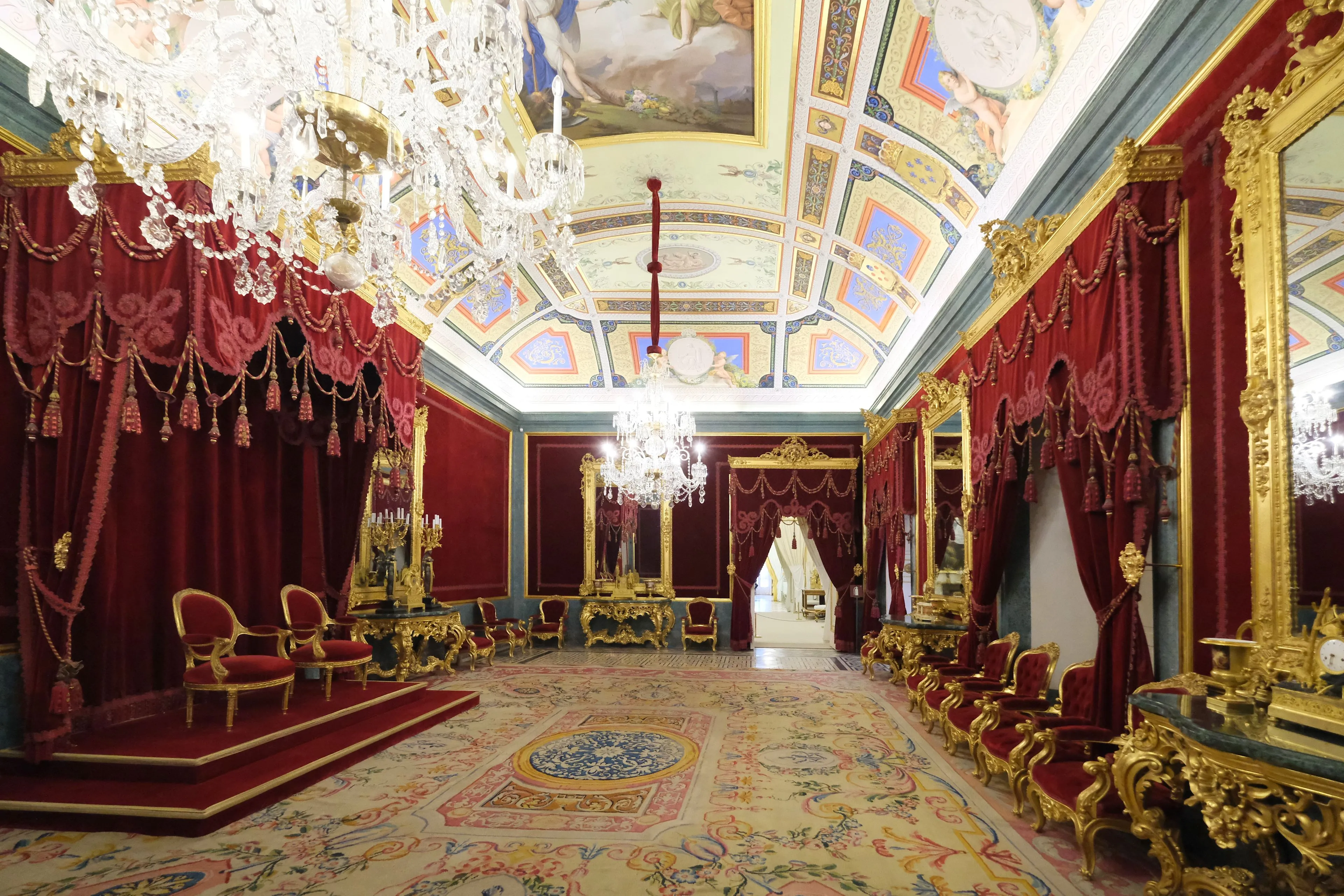 Opulenta sala del trono con cortinas de terciopelo rojo, muebles dorados, una gran lámpara de araña y un techo pintado