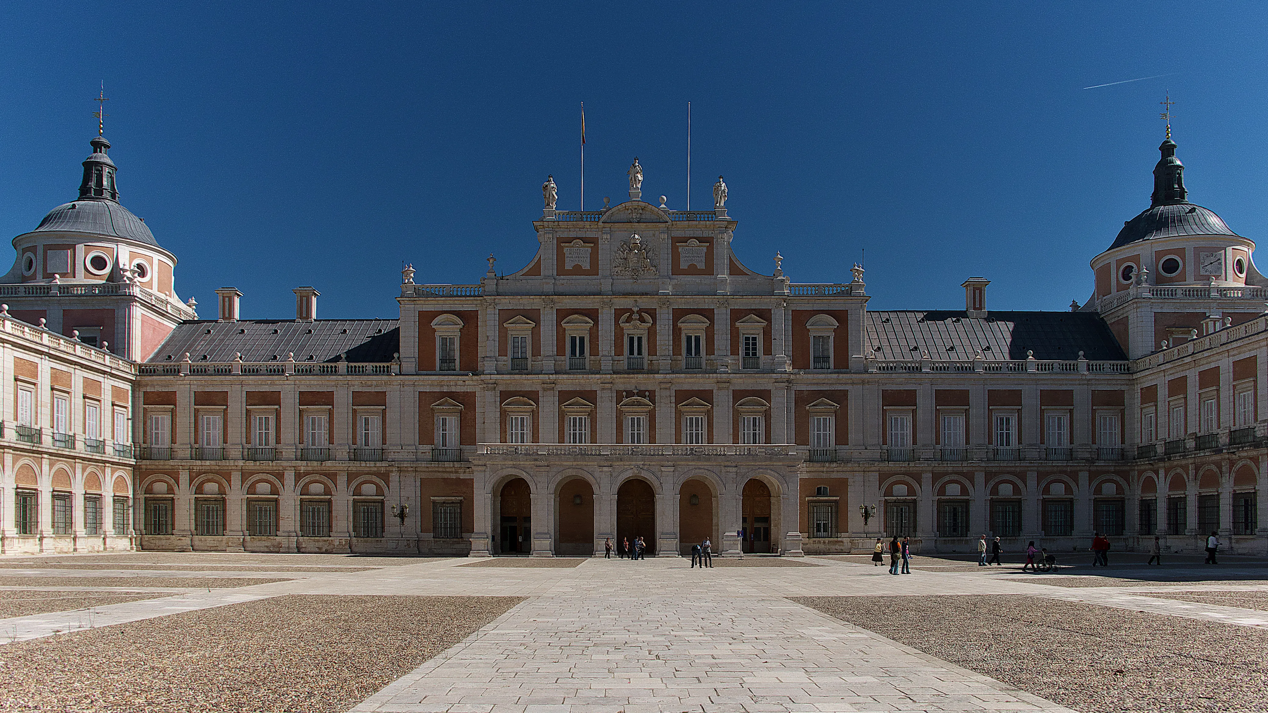 El Palacio Real de Aranjuez con su fachada ornamentada, torres gemelas abovedadas y patio central bajo un cielo azul claro