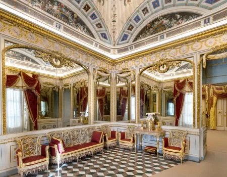 Habitación interior ornamentada con espejos dorados, sillas de terciopelo rojo y suelo ajedrezado