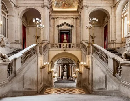 Grote trap in het Koninklijk Paleis van Madrid met sierlijke balustrades, kroonluchters en een centraal standbeeld op de bordes.