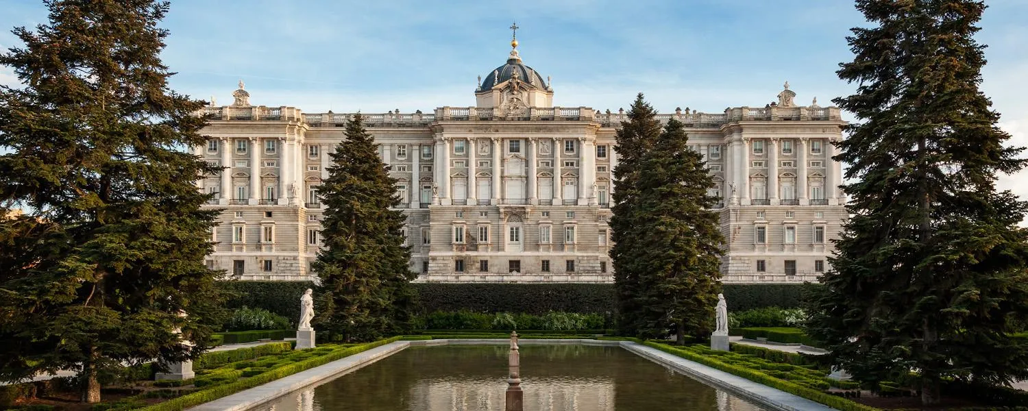 Het Koninklijk Paleis van Madrid met een lange spiegelvijver en groenblijvende bomen op de voorgrond