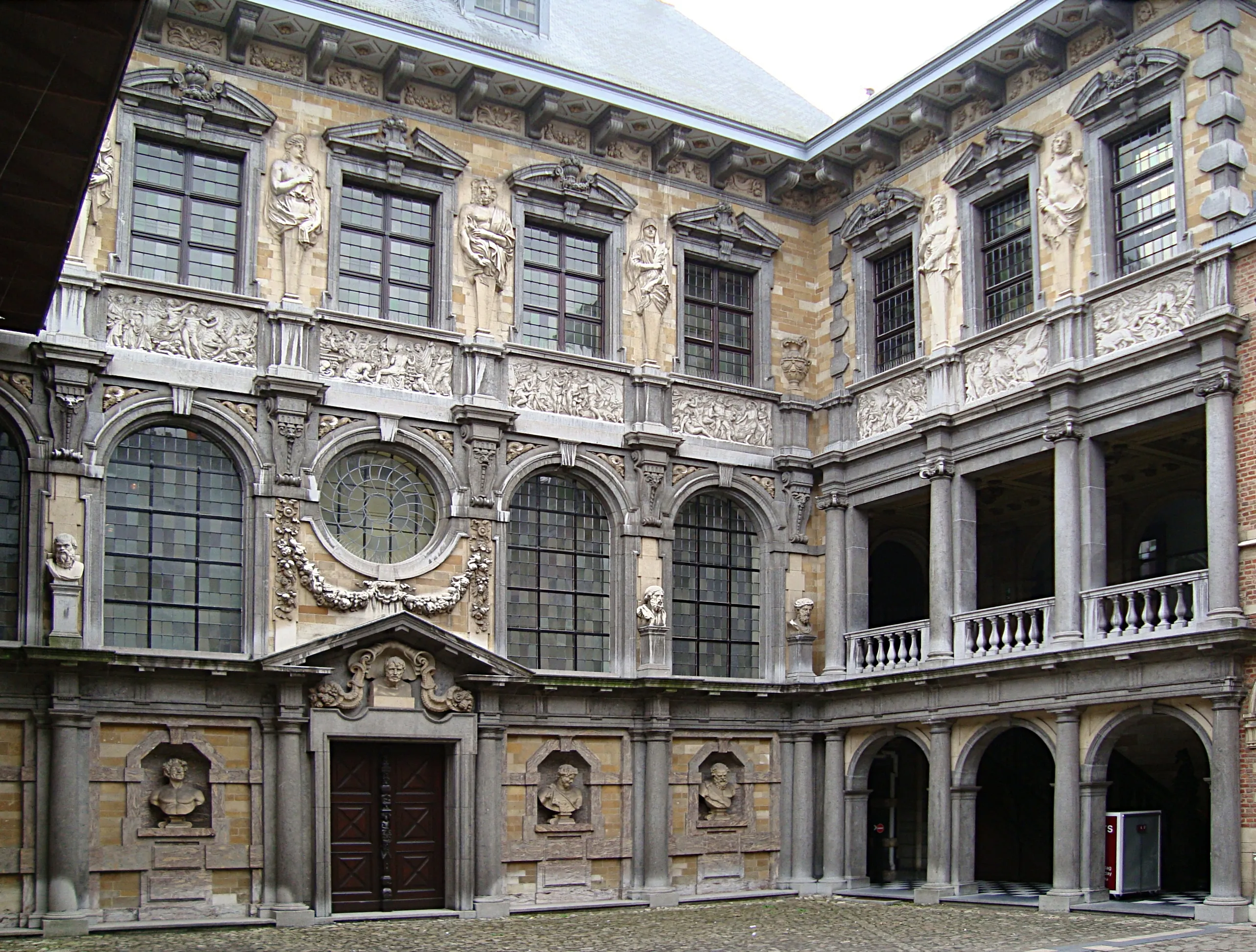Ornado patio barroco del Rubenshuis que presenta fachadas esculpidas, ventanas arqueadas y un pasillo con columnas.