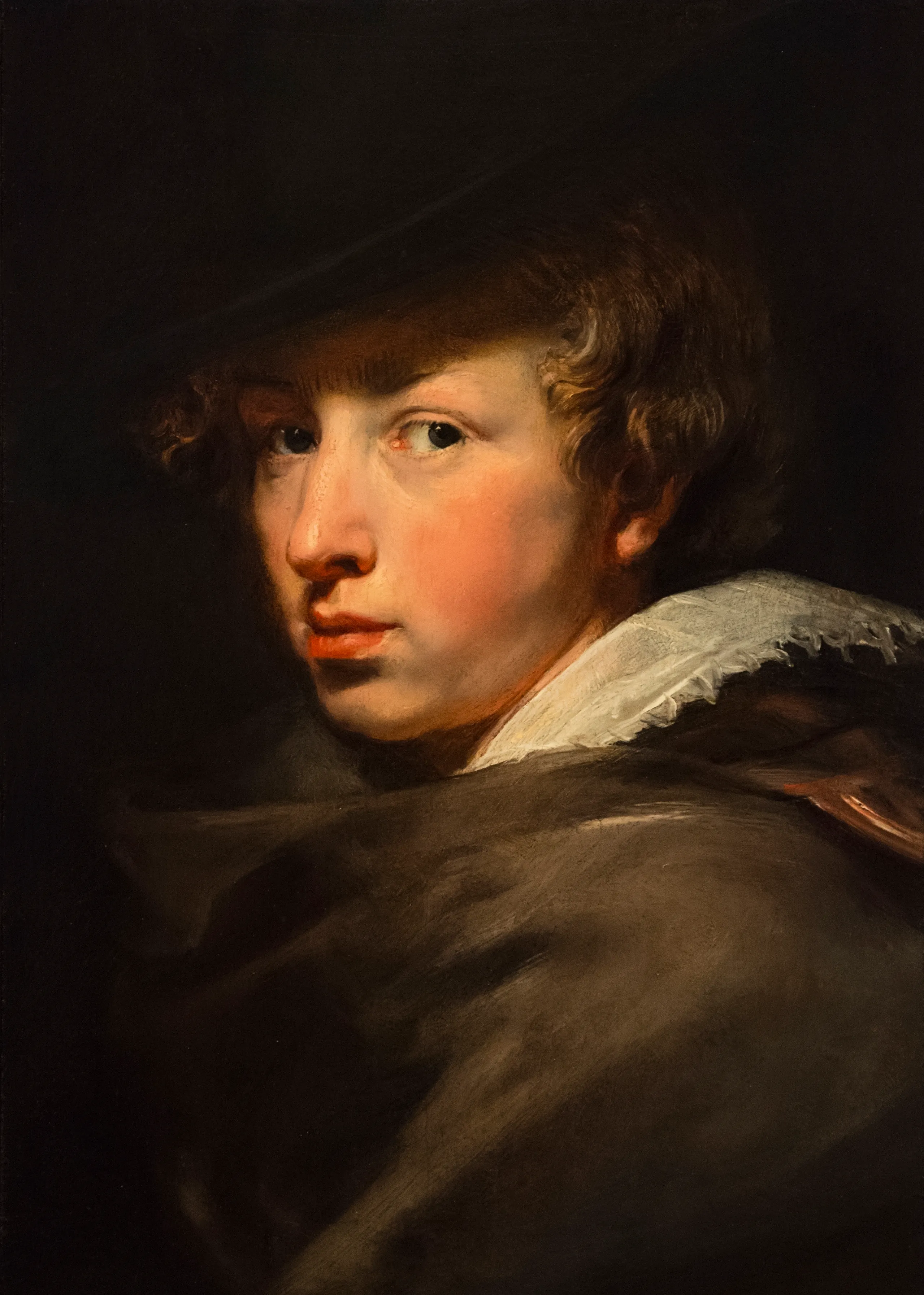 Retrato al óleo de un hombre joven con cabello rizado, que lleva un sombrero de ala ancha y una capa oscura con un cuello de encaje blanco, mirando por encima del hombro sobre un fondo oscuro.