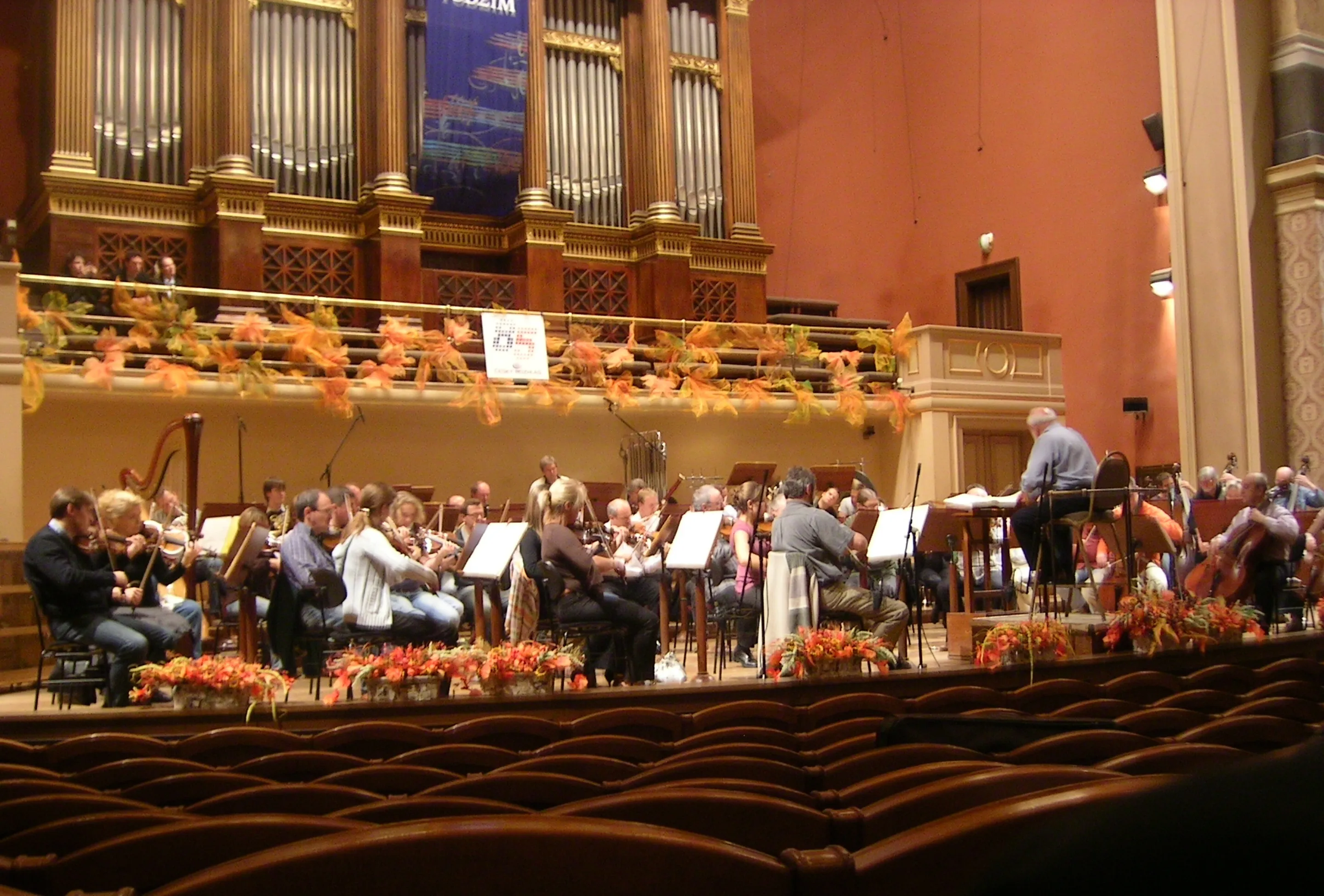 Orquesta actuando en el escenario en una sala de conciertos con un gran órgano de tubos y decoraciones de otoño
