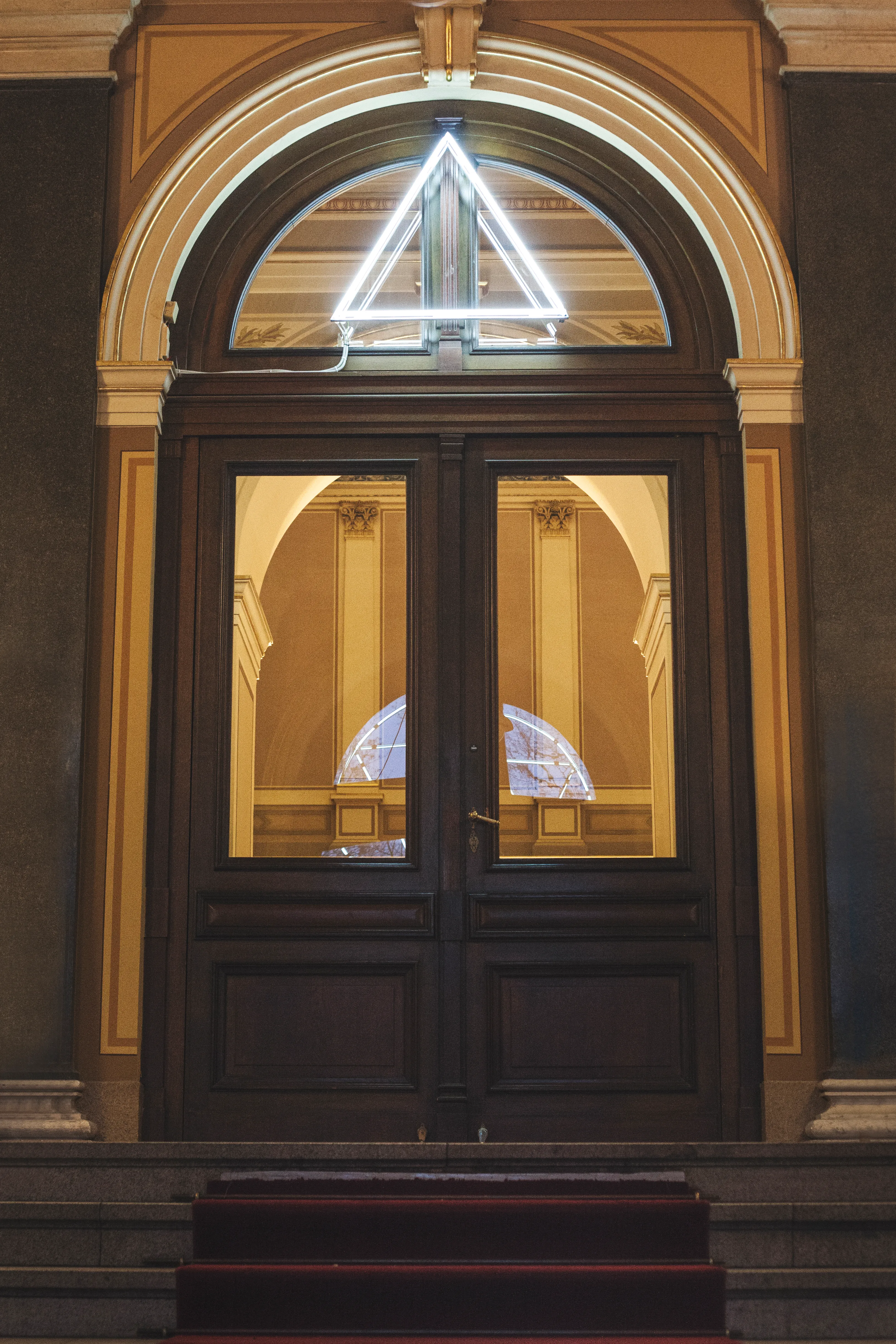 Instalación de luz triangular de neón sobre la puerta de entrada arqueada de madera de la Galerie Rudolfinum