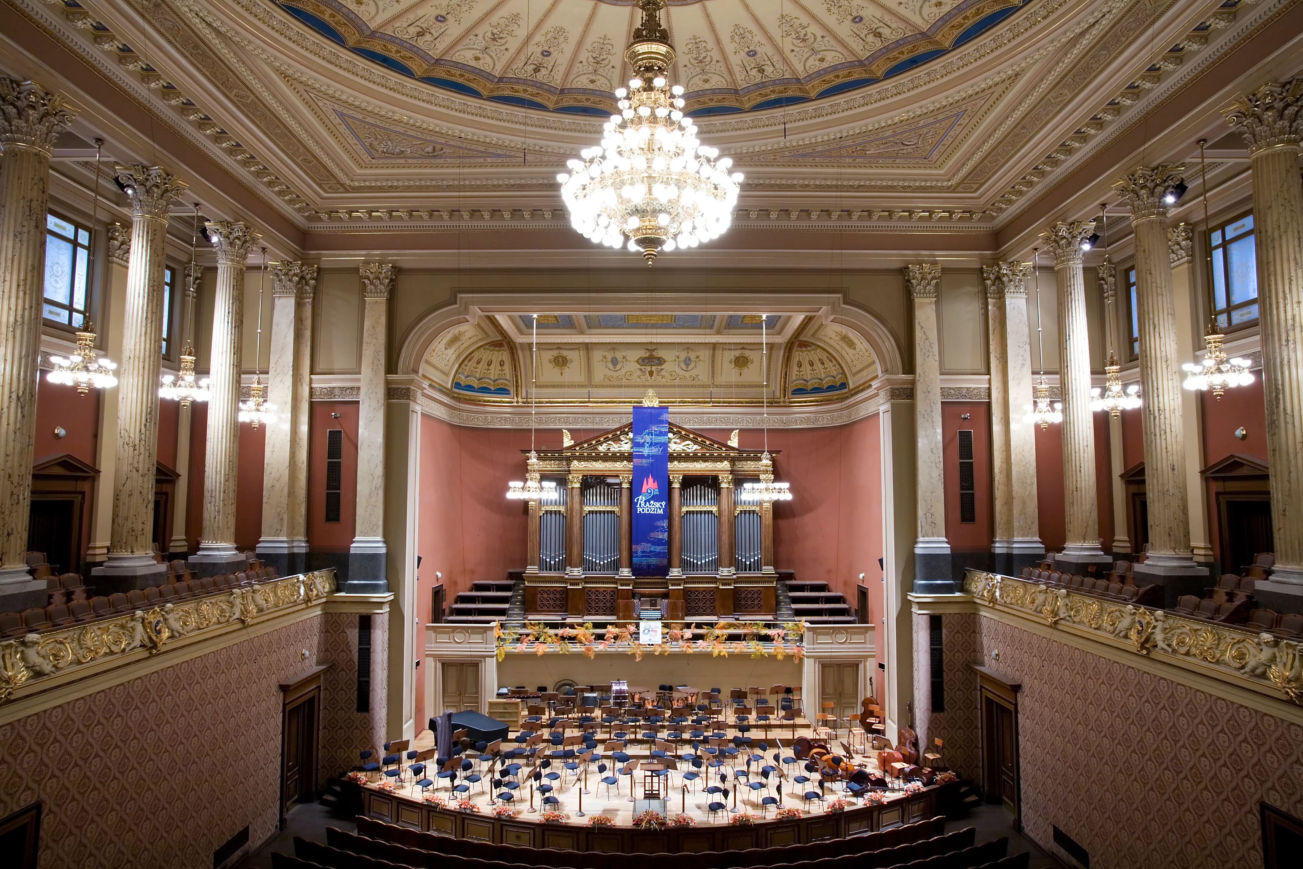 Interior ornamentado de sala de conciertos con columnas, candelabro y órgano