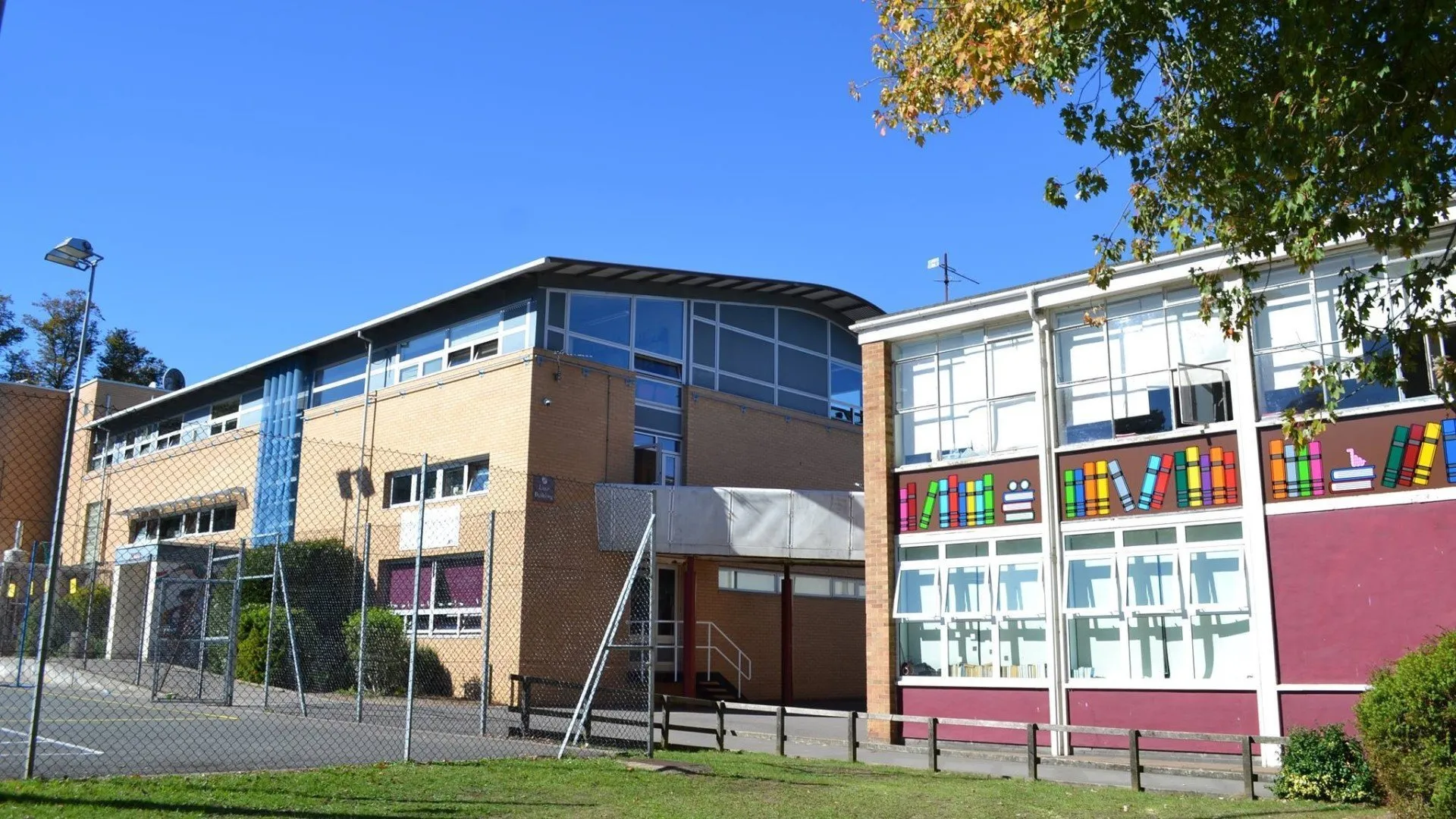 Widok z zewnątrz na budynek Cheney School z kolorowym muralem na ceglanej fasadzie pod bezchmurnym, błękitnym niebem