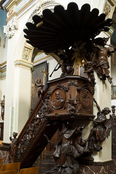 Púlpito de madera oscura ornamentado con tallas elaboradas, figuras religiosas esculpidas y un gran dosel en forma de abanico dentro del interior de una iglesia
