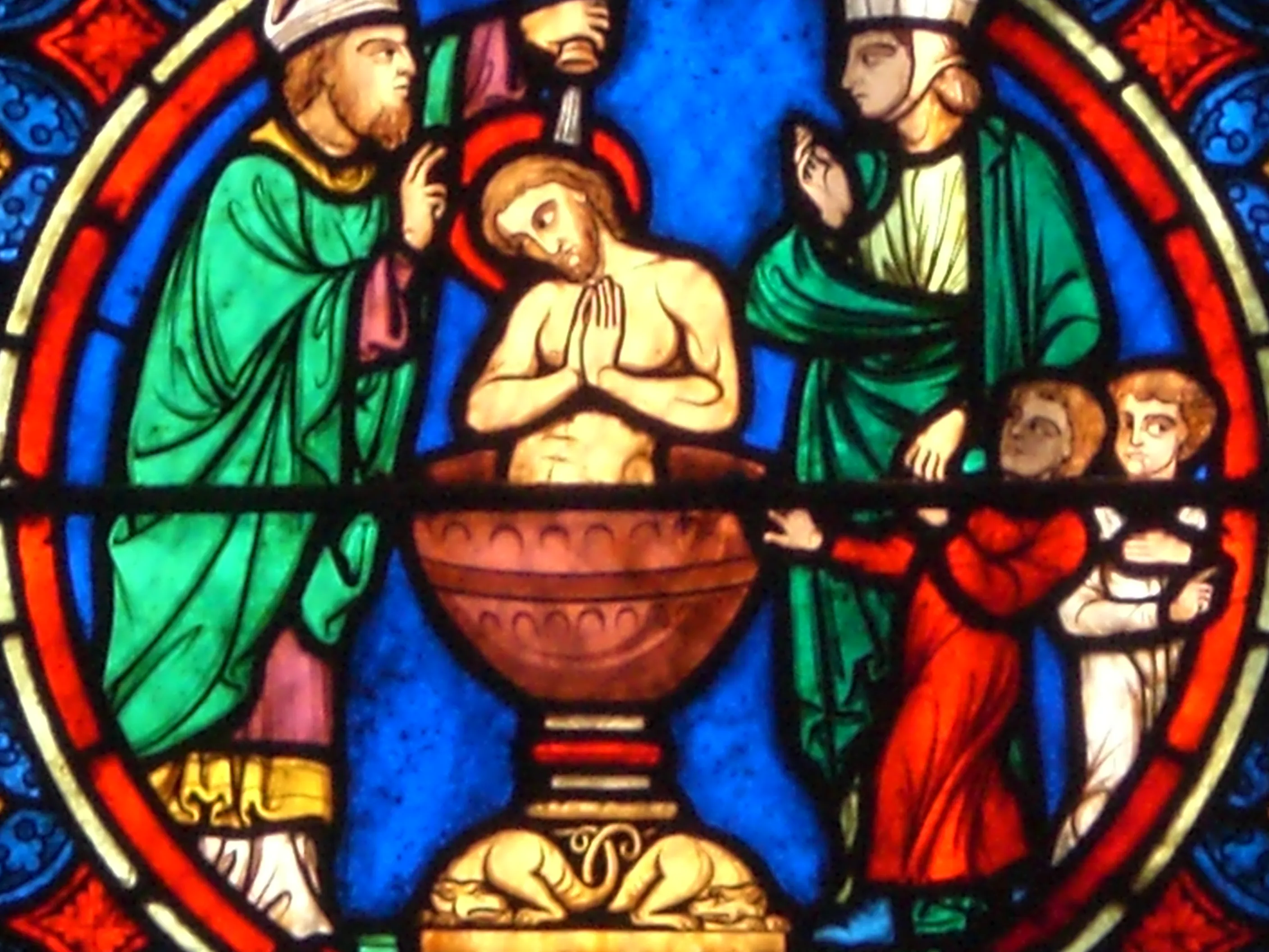 Panel de vidriera que representa el bautismo de Cristo con figuras con túnicas verdes y rojas alrededor de una figura central en una pila bautismal.
