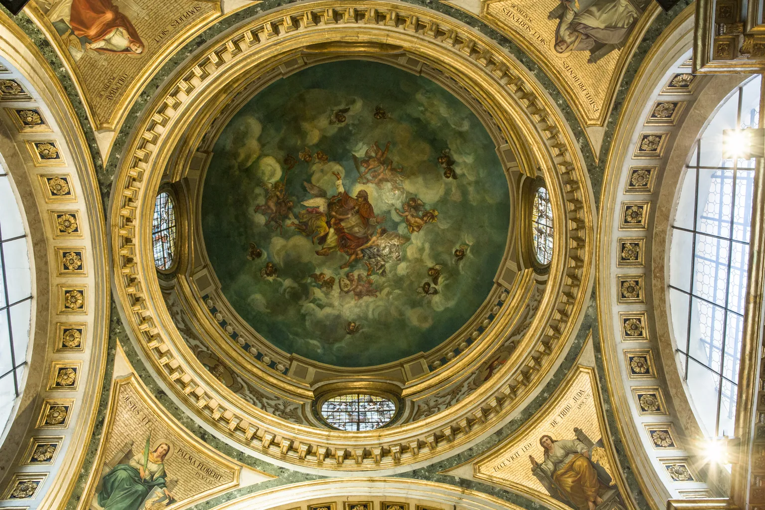 Vista hacia arriba de un techo abovedado ornamentado con un fresco central de figuras en el cielo, rodeado de molduras doradas y ventanas arqueadas.