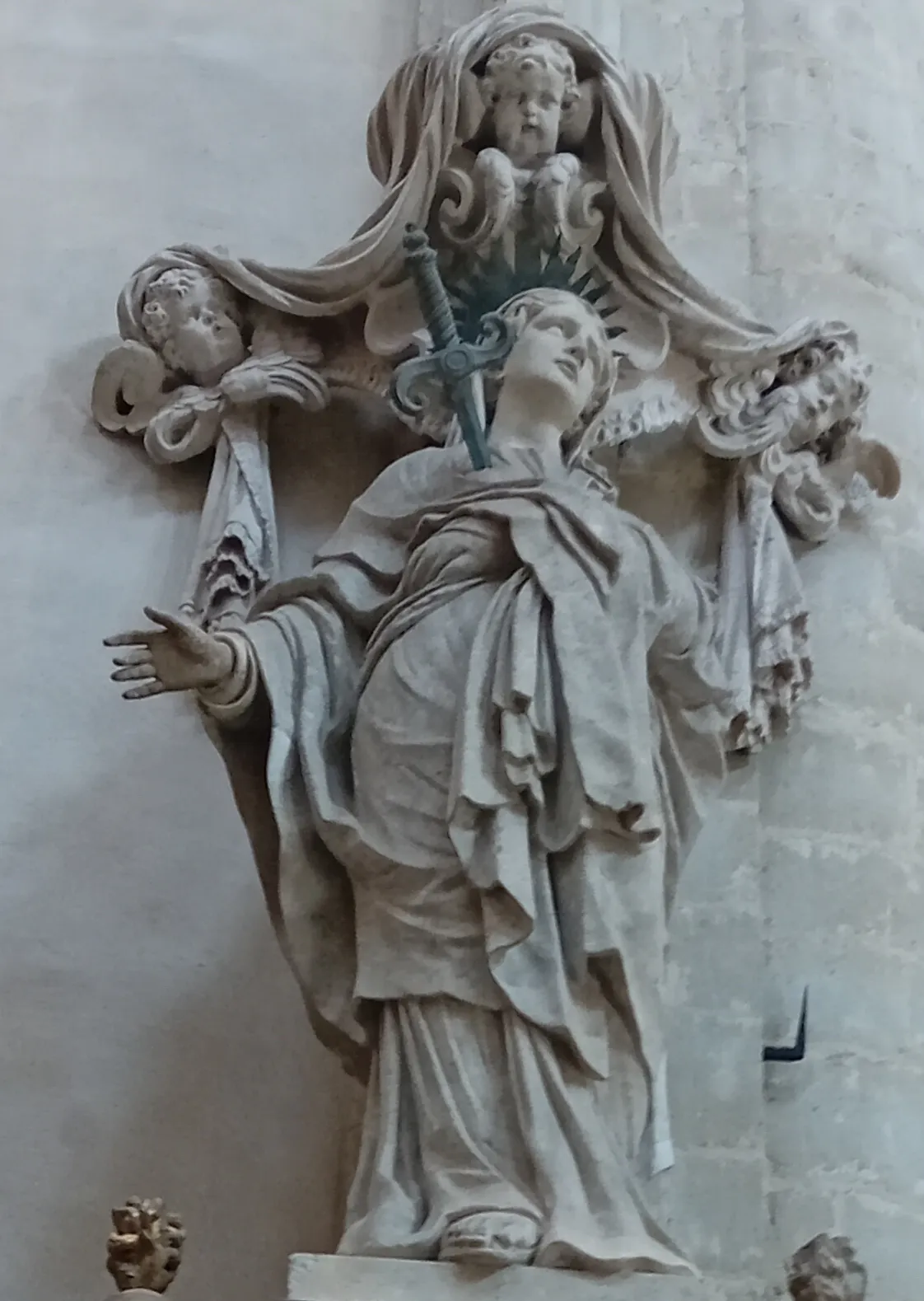 Escultura de piedra de la Virgen María atravesada por una espada, flanqueada por figuras de querubines con drapeados fluidos, dentro de la iglesia de San Andrés