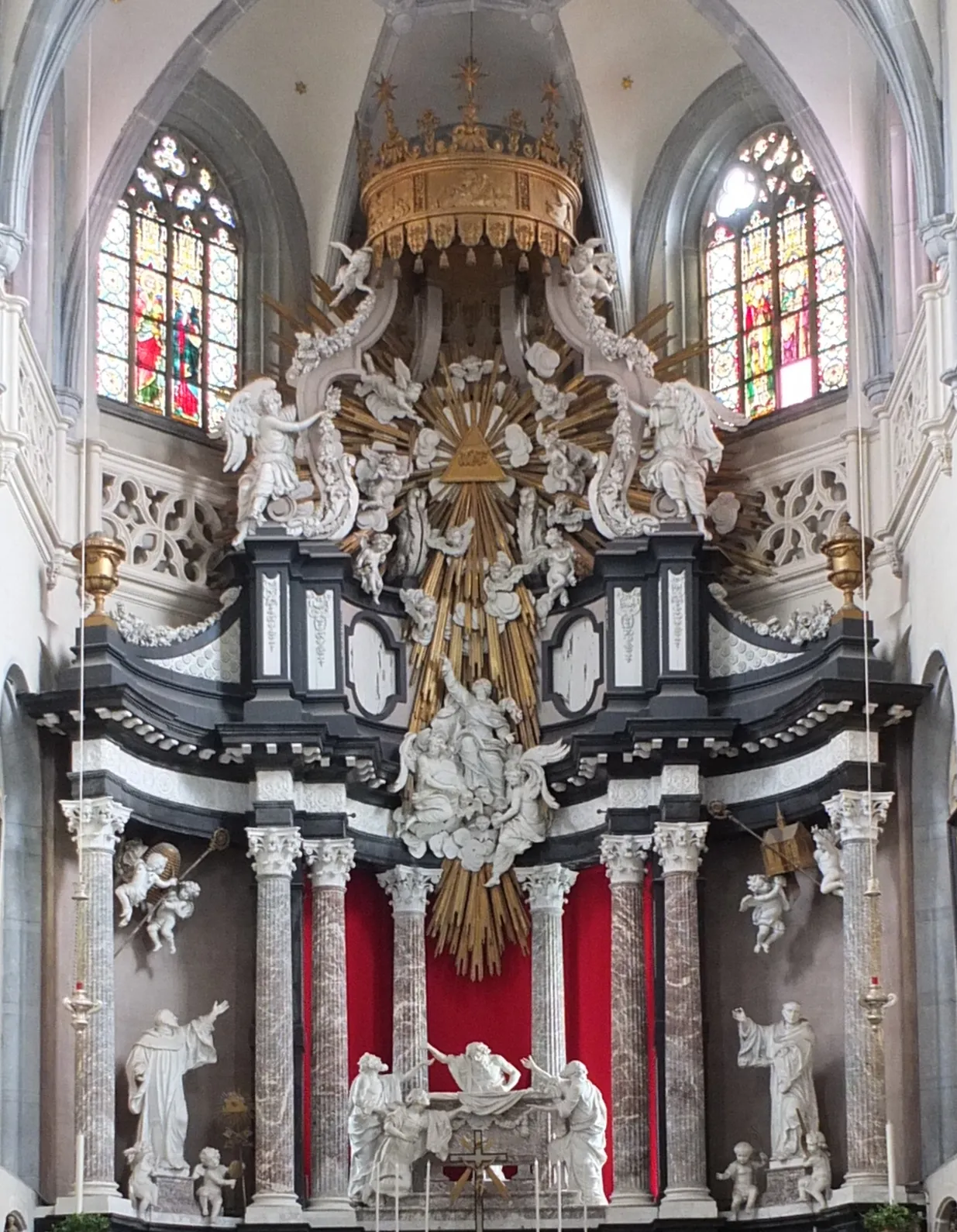 Elaborado altar mayor barroco con esculturas de mármol blanco, columnas corintias, dosel dorado y cortinajes rojos en la iglesia de San Andrés, con vidrieras encima.