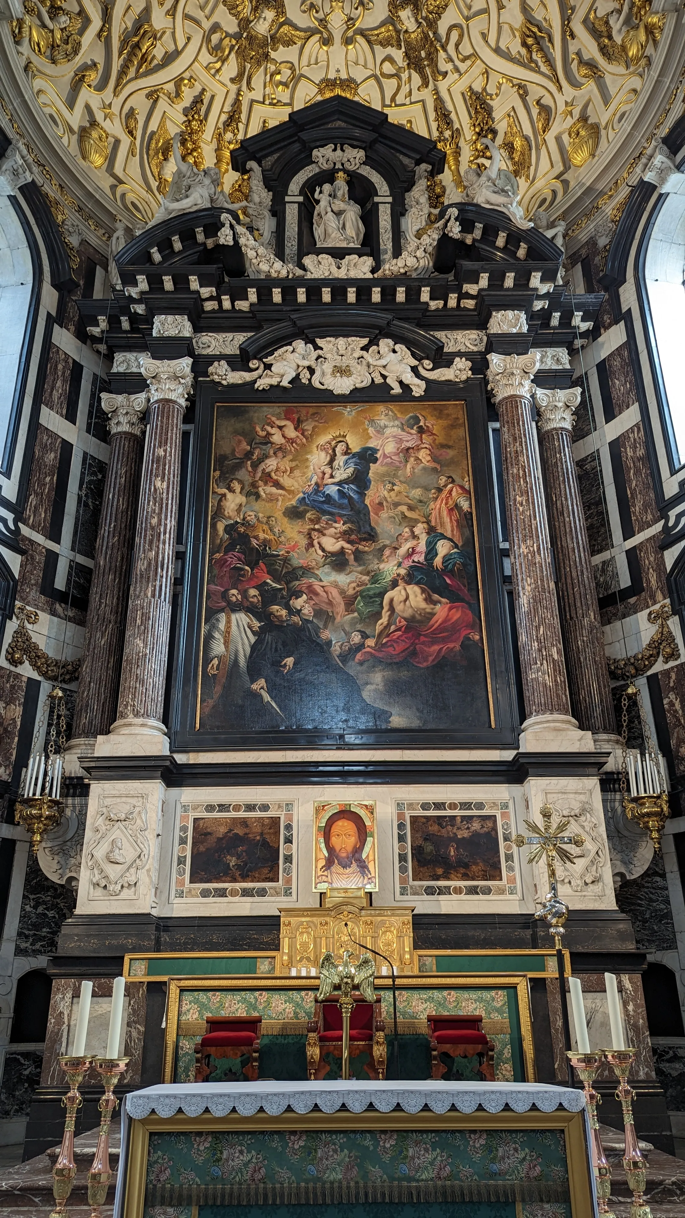 Rijkversierd barokaltaar met een groot religieus schilderij dat de Maria-Tenhemelopneming verbeeldt, geflankeerd door marmeren zuilen en bekroond met standbeelden, onder een verguld stucwerkplafond in de Sint-Carolus Borromeuskerk