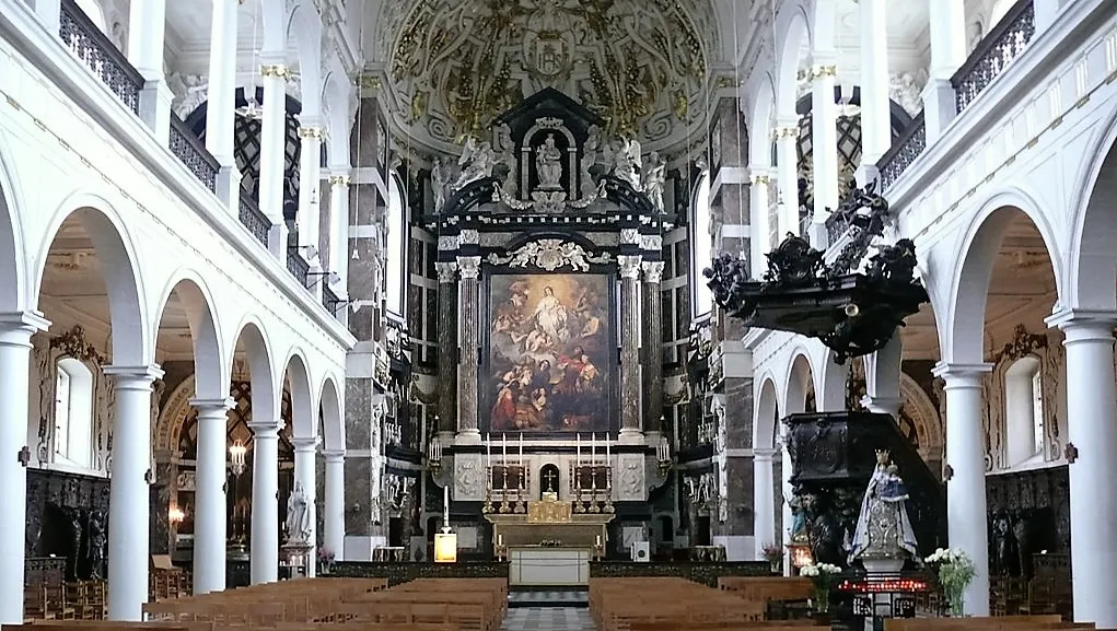 Interieur van de Saint Charles Borromeo Church met zicht op het schip, witte zuilen, bogen en het rijk versierde altaar met een groot schilderij.