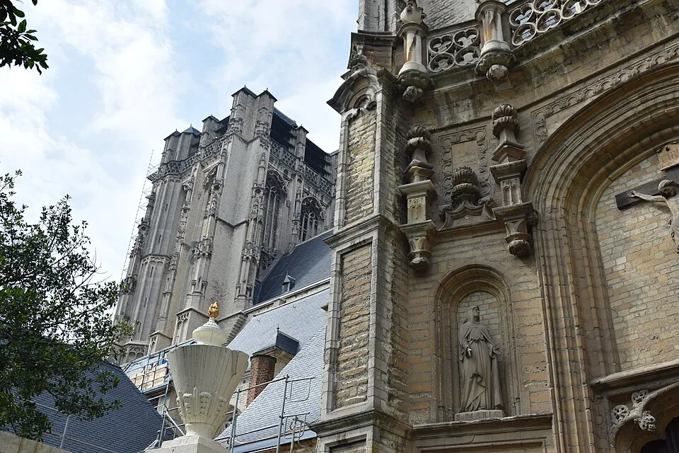 Fachada de piedra de la iglesia de Santiago con torre gótica bajo andamios, hornacina barroca con estatua y urna de piedra blanca en primer plano