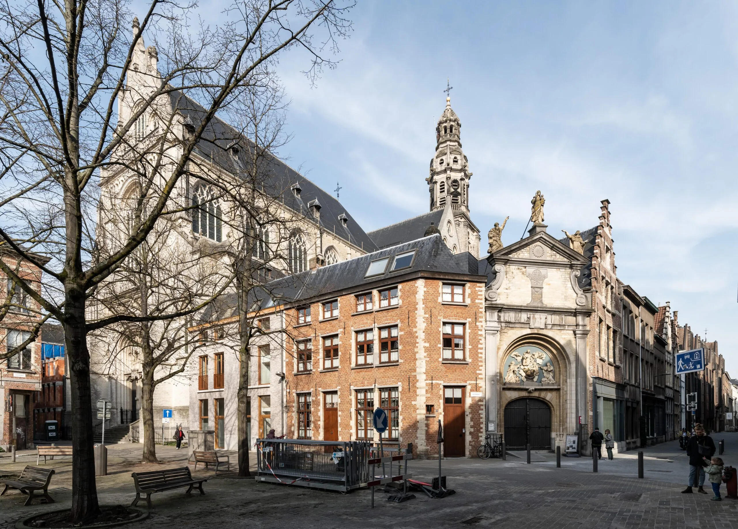 Vista exterior de la Saint Paul's Church que muestra su fachada de piedra gótica, el edificio anexo de ladrillo, la ornamentada puerta de entrada barroca con estatuas y la plaza circundante con árboles desnudos