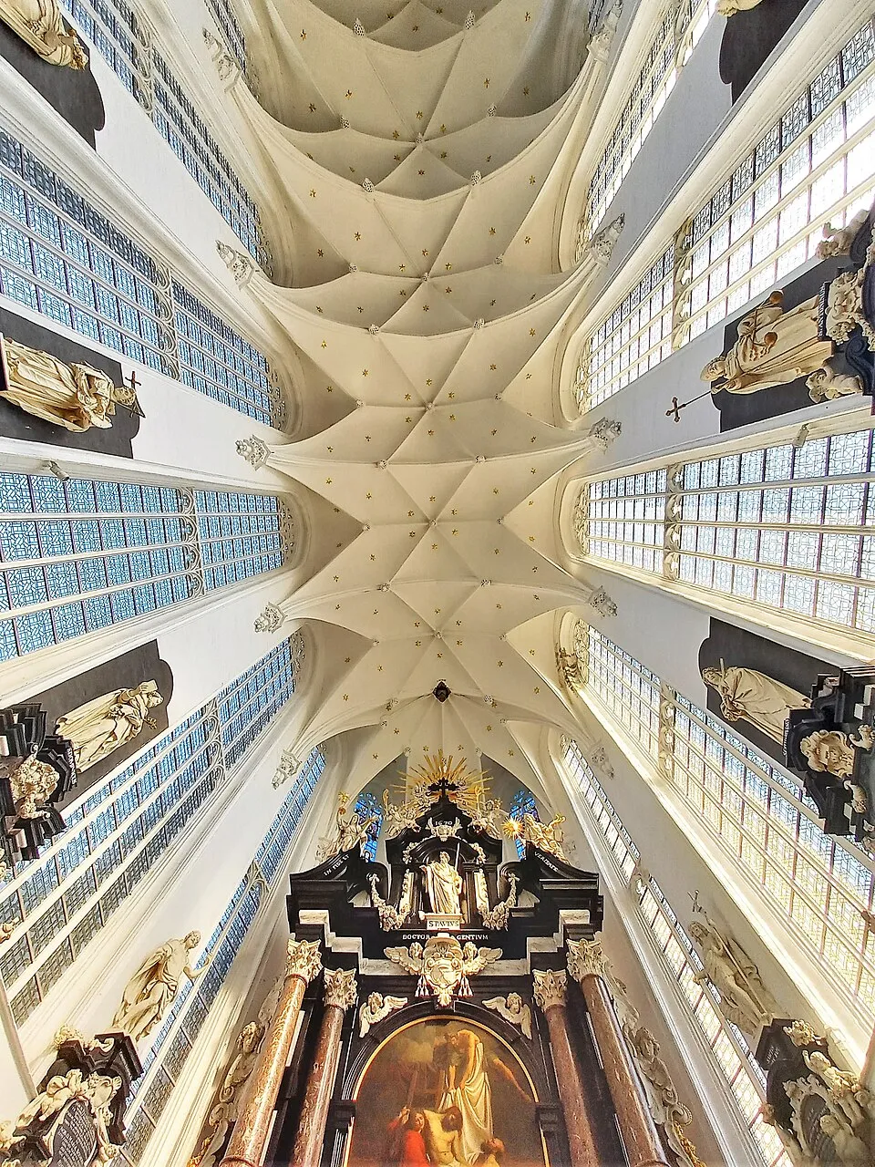 Vista desde un ángulo bajo mirando hacia arriba al techo abovedado de nervaduras blancas y a la nave de la Saint Paul's Church, que conduce a un altar barroco con estatuas y una pintura.