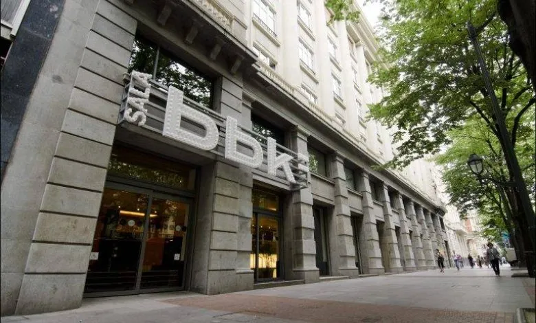 Vista a pie de calle de la fachada del edificio Sala BBK con letras blancas grandes sobre la entrada, columnas de piedra y un paseo peatonal arbolado.