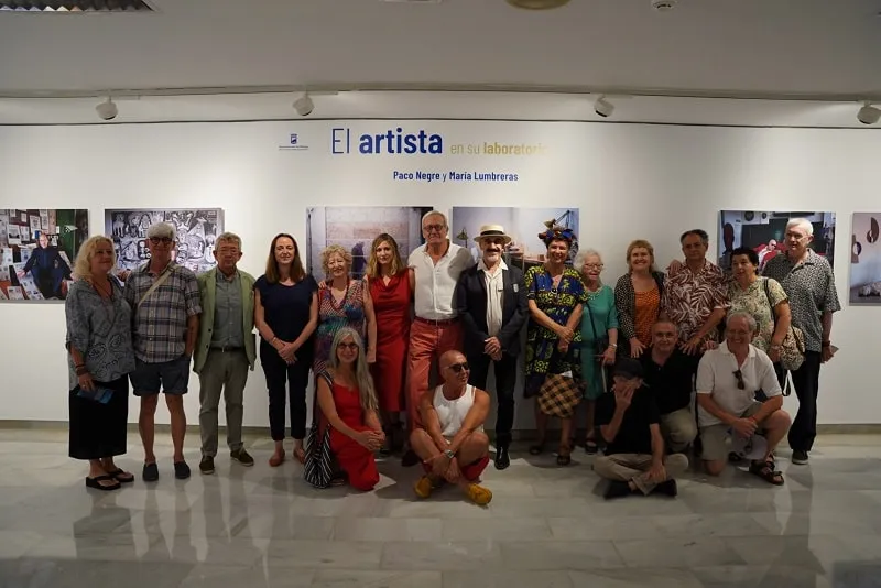 Grupo de personas posando frente a un muro de exposición que reza 'El artista y su trabajo — Paco Negro y María Zambrano' dentro del espacio expositivo Salas Mingorance.