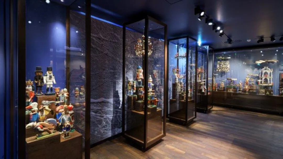 Sala de museo con iluminación tenue y vitrinas de cristal que exhiben figuritas navideñas y cascanueces bajo focos.