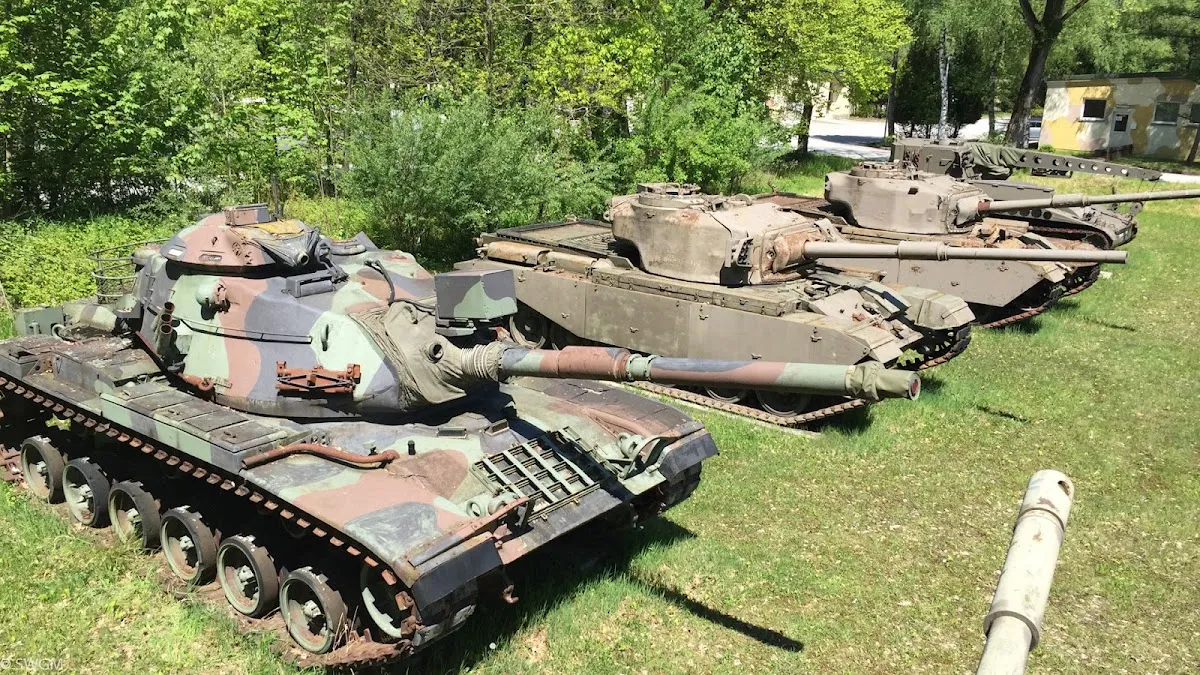 Three camouflaged military tanks displayed in a row on a grassy outdoor area with trees in the background