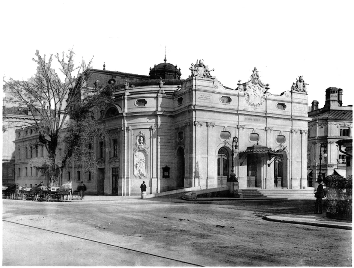 Historical black and white photograph of the Salzburg State Theatre exterior showing the ornate facade, entrance, and street with horse-drawn carriages.