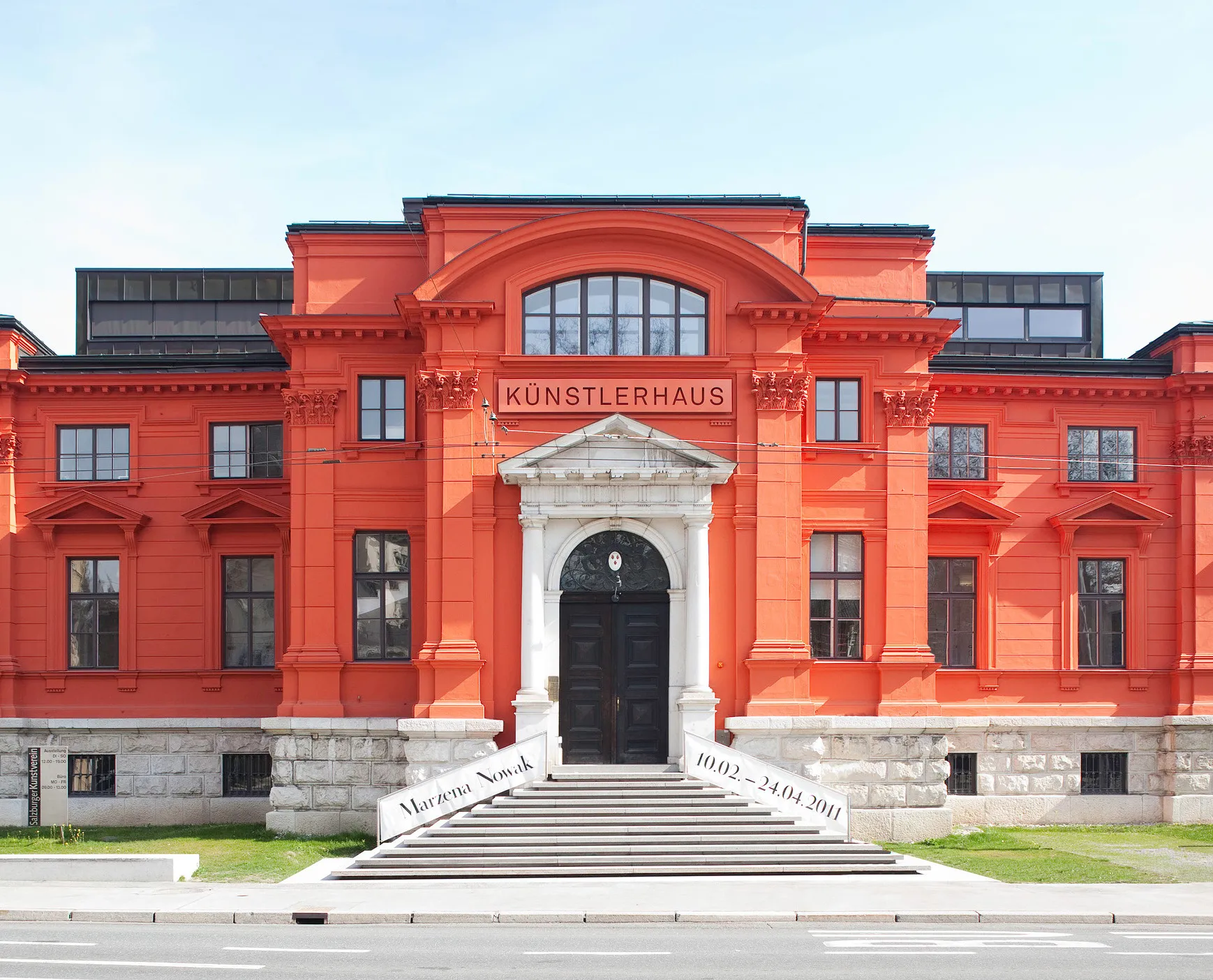 Fachada del edificio Künstlerhaus de color rojo anaranjado brillante con entrada clásica de arco, escalones de piedra y grandes ventanales bajo un cielo azul