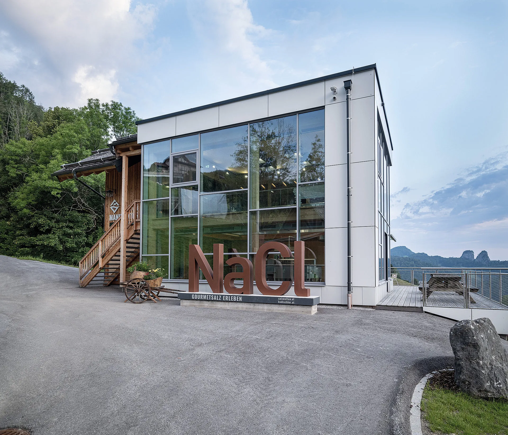 Edificio moderno de fachada de cristal con grandes letras marrones de NaCl en la parte delantera, una escalera de madera a la izquierda y montañas visibles al fondo