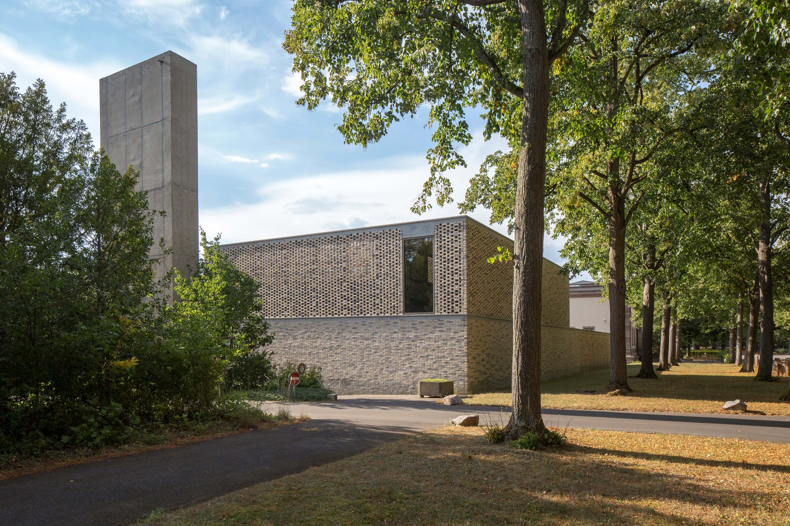 Modern bakstenen gebouw met een hoge betonnen toren, omringd door bomen en een verhard pad bij het Sammlung Friedhof Hörnli begraafplaatsmuseum