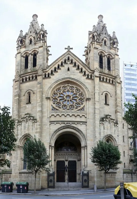 Neogotische kerkgevel met twee klokkentorens, een groot roosvenster en een boogvormige ingang aan een stadsstraat
