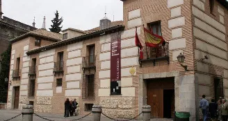 Edificio histórico con fachada de piedra, balcones de madera y una bandera española sobre la entrada