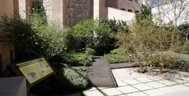 patio ajardinado con pasarela de madera, muros de piedra y cartel informativo en el Museo de San Isidro