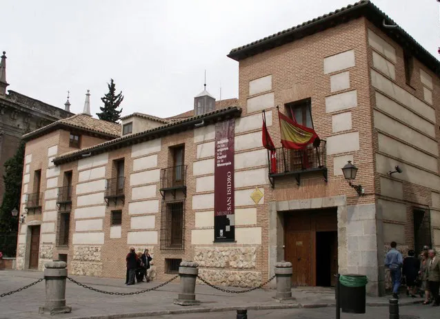 Exterior del Museo de San Isidro con fachada beige y blanca, balcones de madera y una bandera española